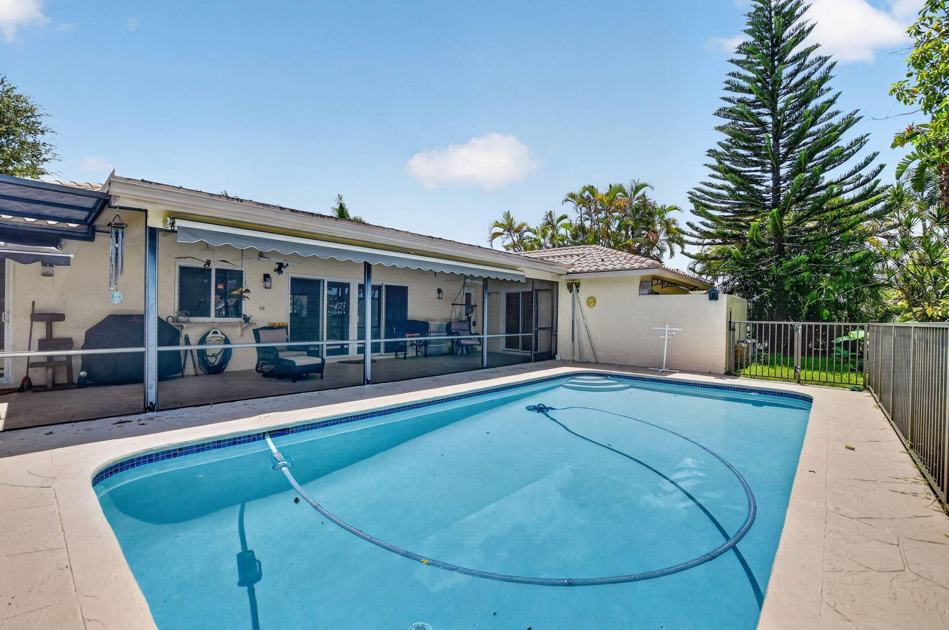 Rectangular swimming pool with tiled coping, screened patio with awning, and a tile roof