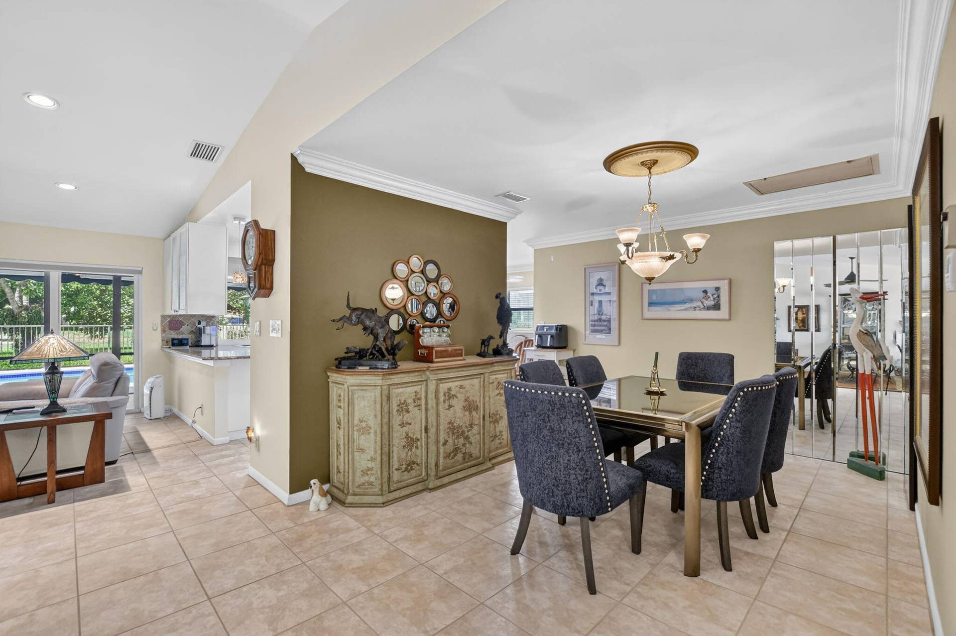 Open concept living and dining areas featuring tile flooring, crown molding, a decorative chandelier, and built-in white cabinetry
