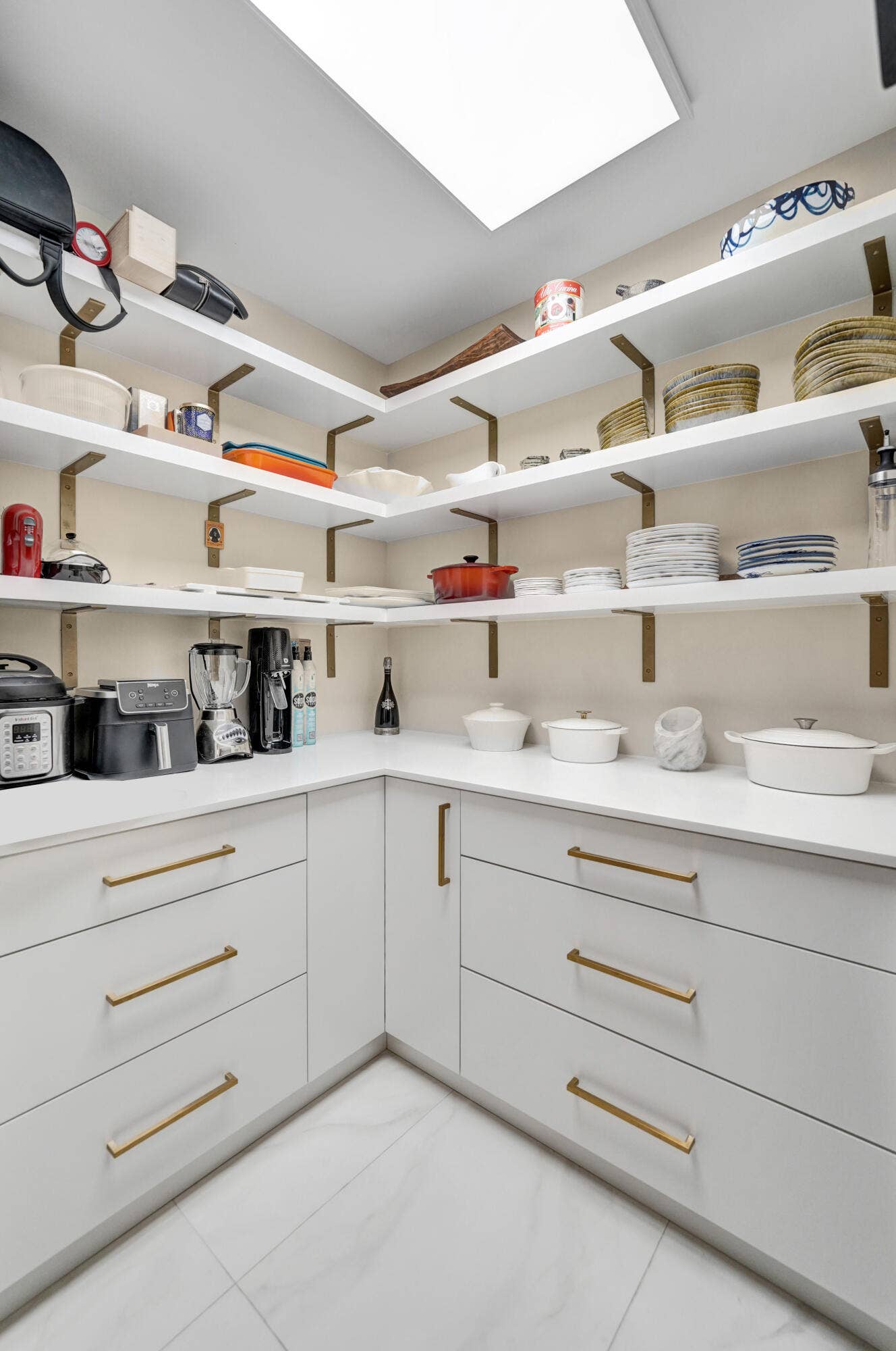 Built-in cabinetry with gold-tone hardware, white countertops, extensive open shelving with gold-tone brackets, and a recessed ceiling light