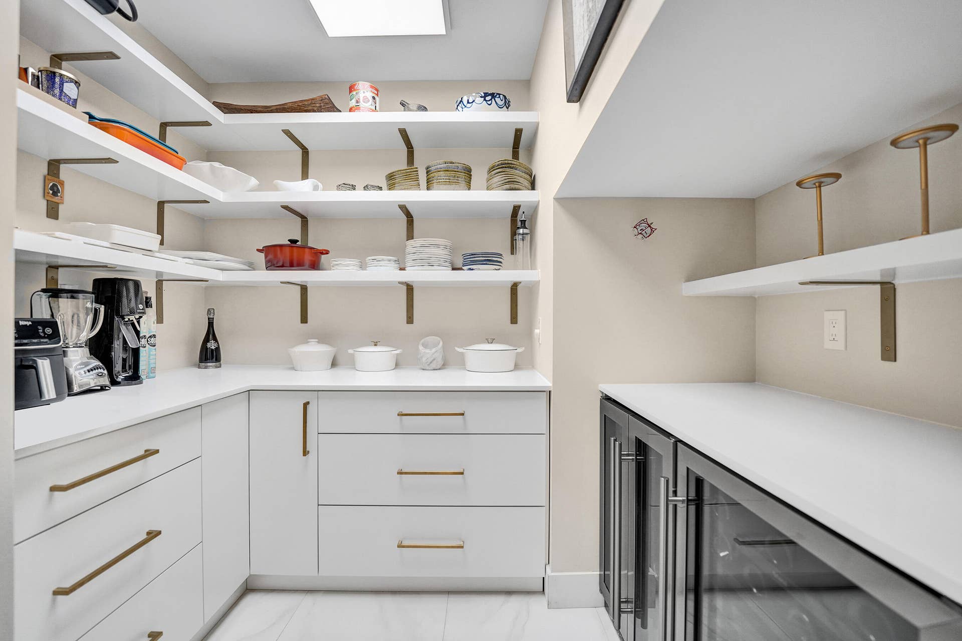 Custom storage pantry featuring white cabinetry, extensive shelving with brass-finish brackets, white countertops, and integrated beverage refrigerators