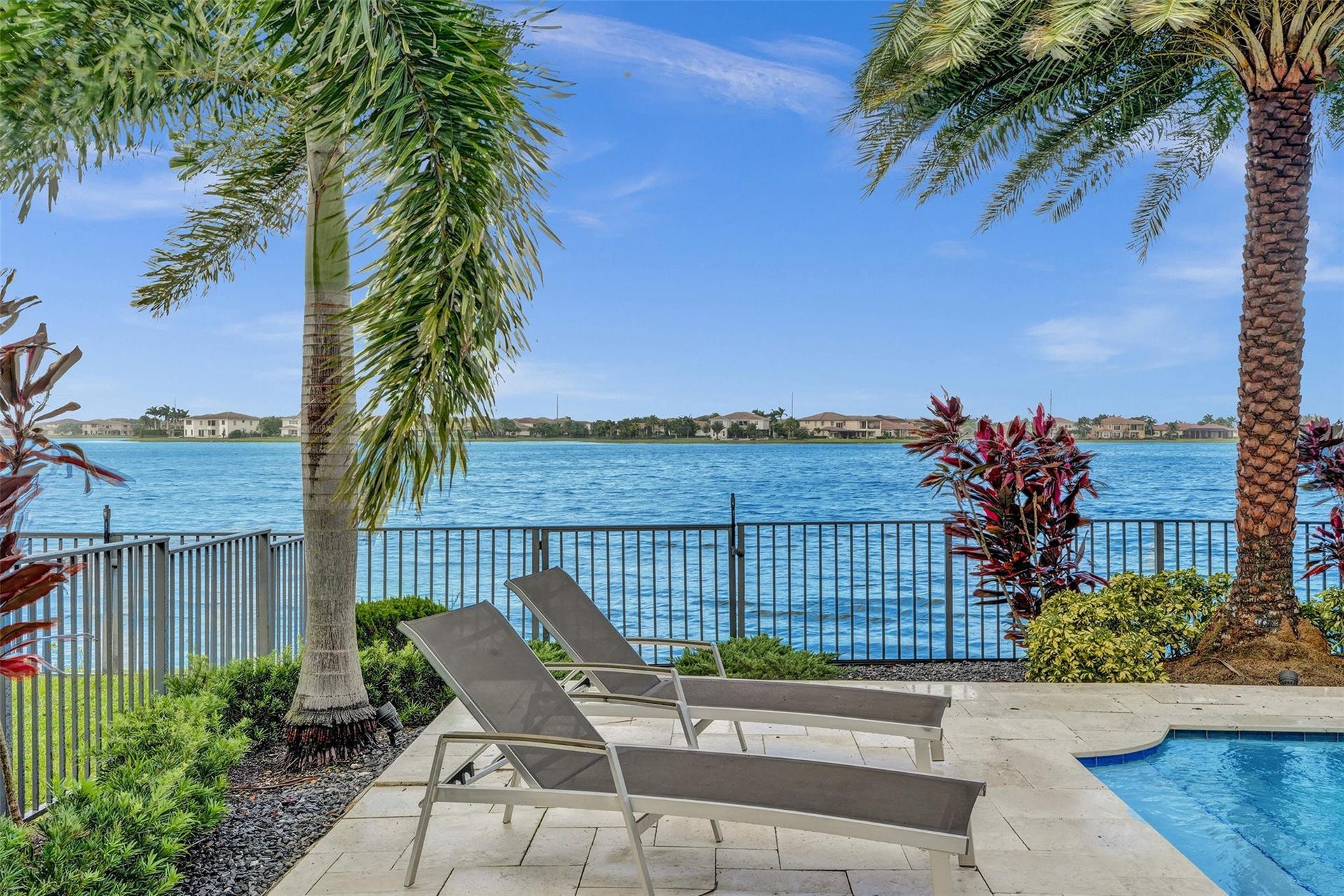 9749 Blue Isle, #BAY, Parkland, FL 33076 Waterfront property featuring a private pool with a curved edge, a metal fence, and mature palm trees