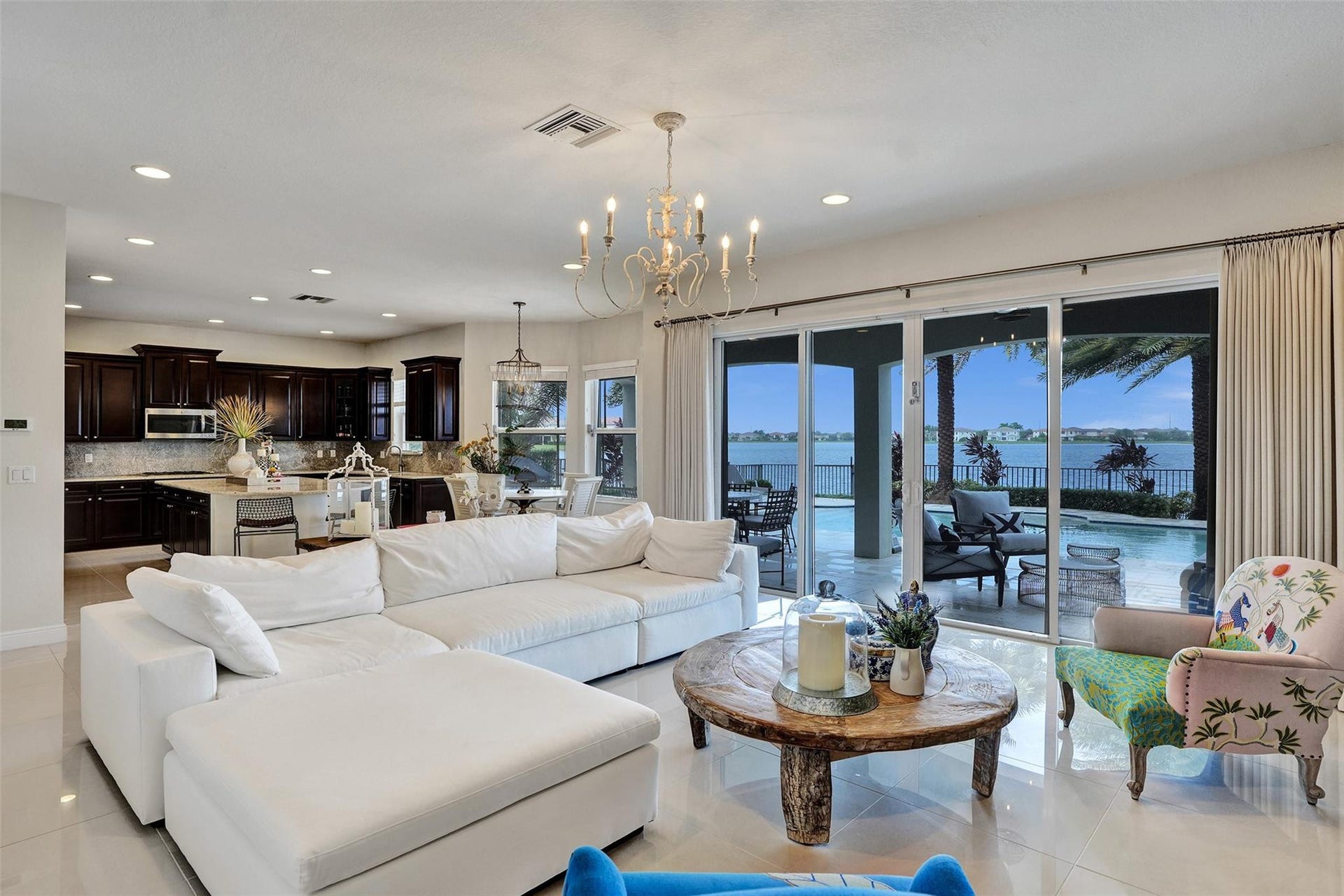 9749 Blue Isle, #BAY, Parkland, FL 33076 Open concept living area with large format tile flooring, a multi-panel sliding glass door, and a built-in kitchen featuring dark wood cabinetry and a tile backsplash