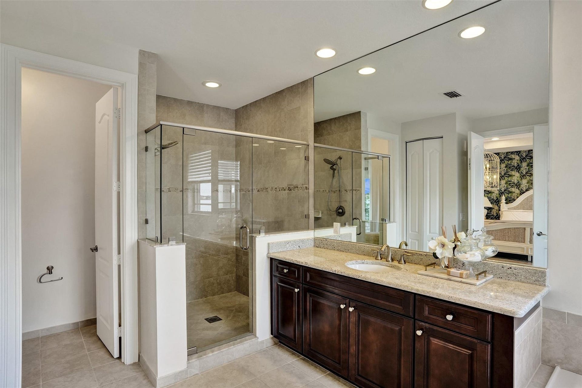 9749 Blue Isle, #BAY, Parkland, FL 33076 Spa-inspired primary bathroom featuring a frameless glass-enclosed walk-in shower with tile surround, dual vanity with wood-finish cabinetry and stone countertop, recessed ceiling lighting, and large mirror with integrated lighting