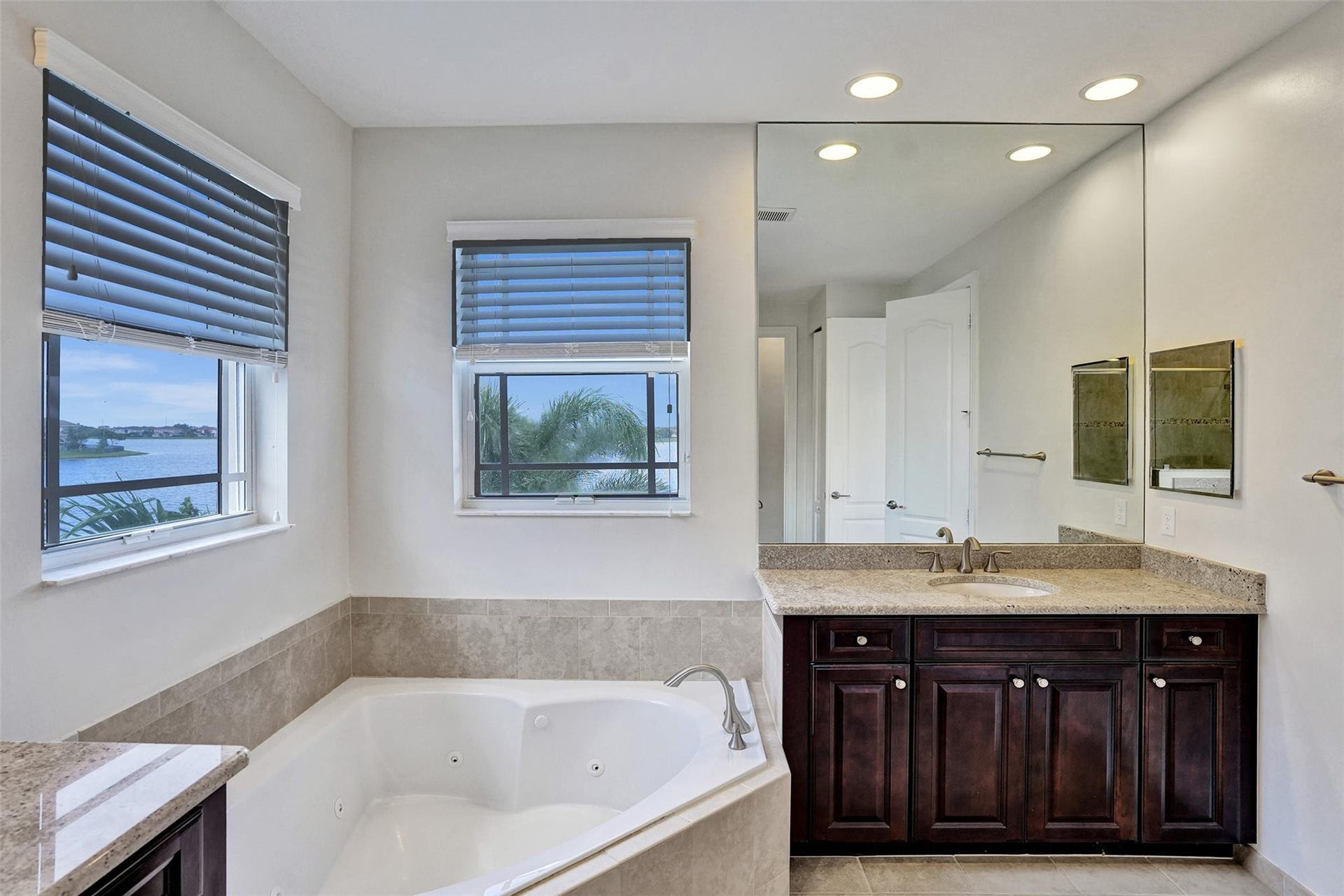 9749 Blue Isle, #BAY, Parkland, FL 33076 Corner soaking tub with integrated jets, dual windows with blinds, built-in vanity with a light-colored countertop, recessed lighting, and a large wall-mounted mirror