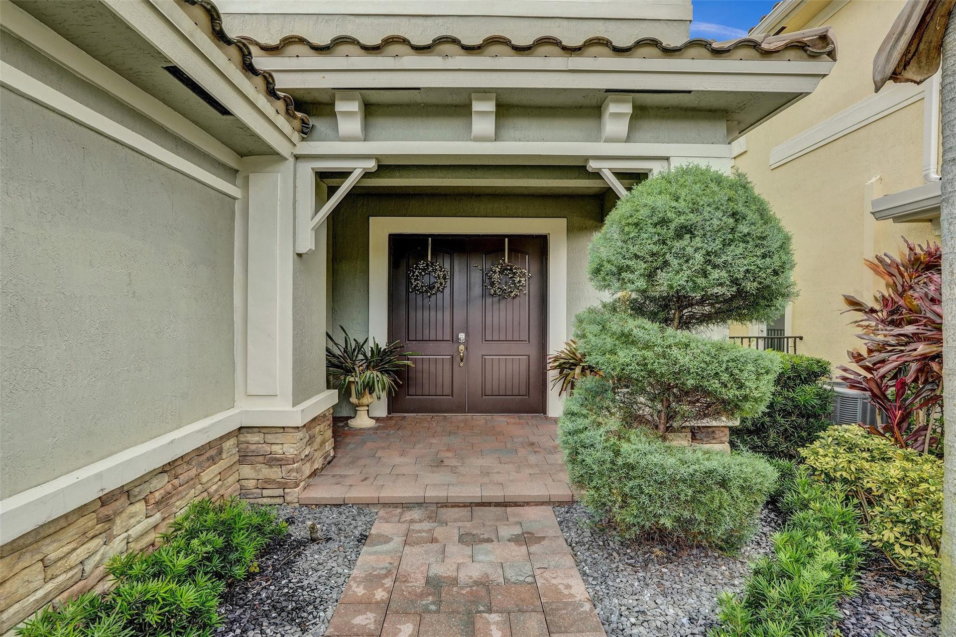 9749 Blue Isle, #BAY, Parkland, FL 33076 Entryway featuring a double wood-paneled door, brick paver walkway, decorative stone veneer, and mature landscaping