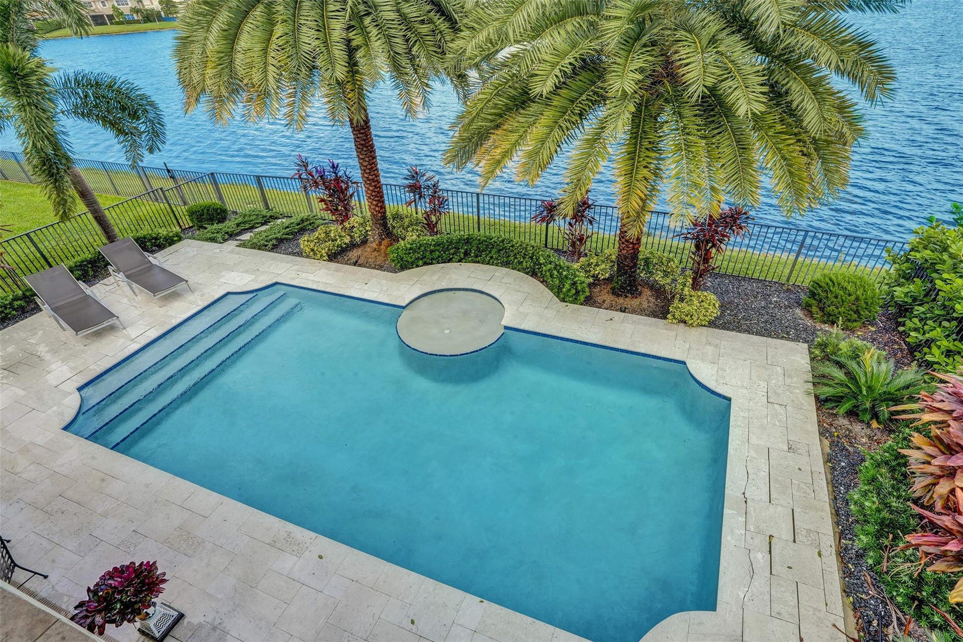 9749 Blue Isle, #BAY, Parkland, FL 33076 Lakeside pool area with a wrought iron fence, palm trees, and stone paver decking