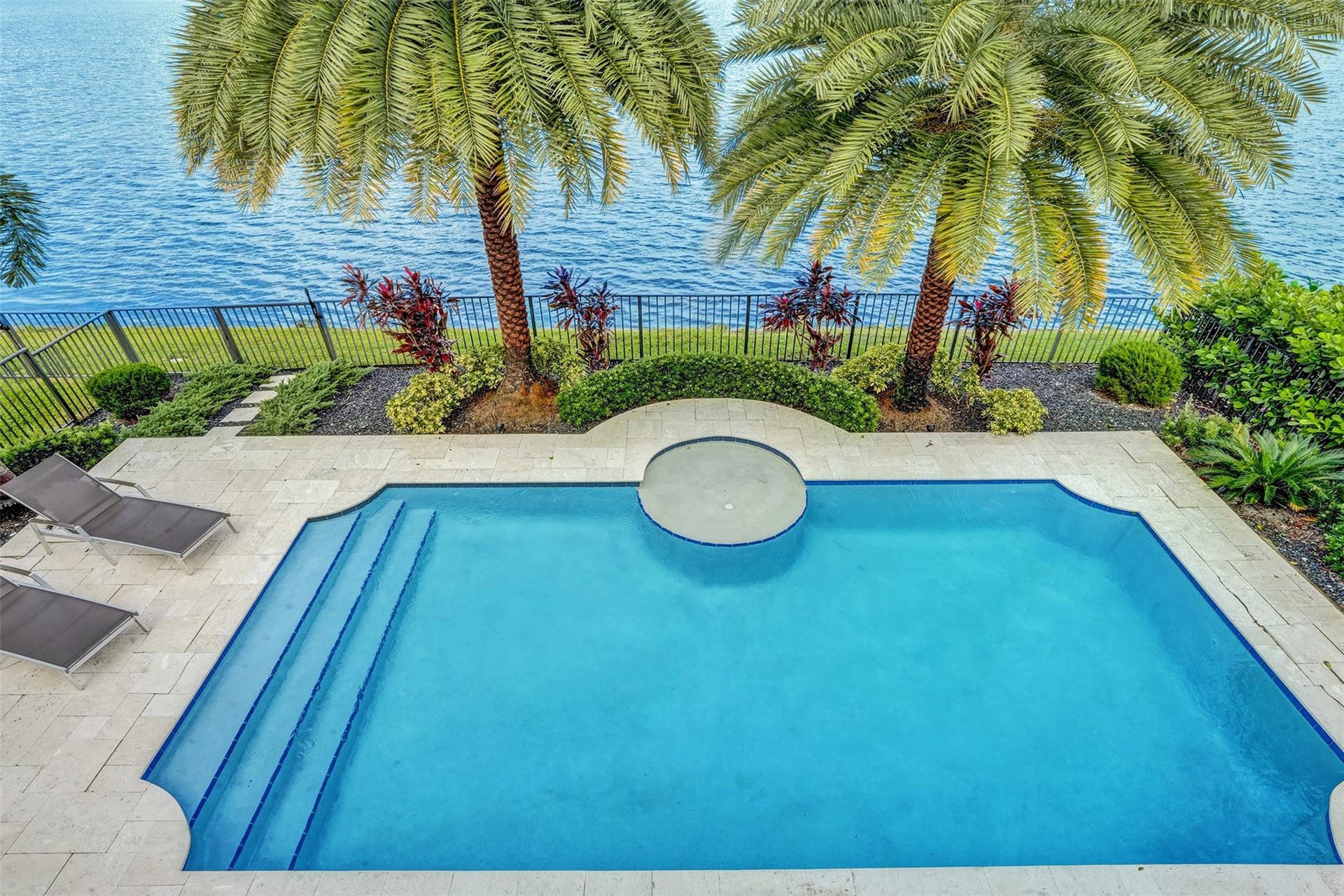 9749 Blue Isle, #BAY, Parkland, FL 33076 Resort-style pool with integrated spa and broad steps, surrounded by a paved patio, lush landscaping, and a secure perimeter fence