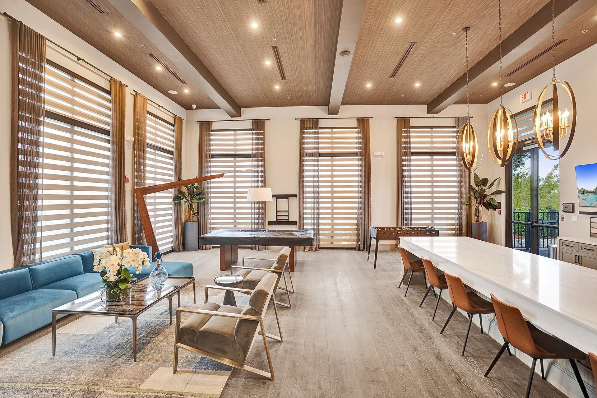 9749 Blue Isle, #BAY, Parkland, FL 33076 Spacious common area featuring wood-finish flooring, a wood-paneled ceiling with recessed lighting, large windows with blinds and drapes, and a long white countertop bar