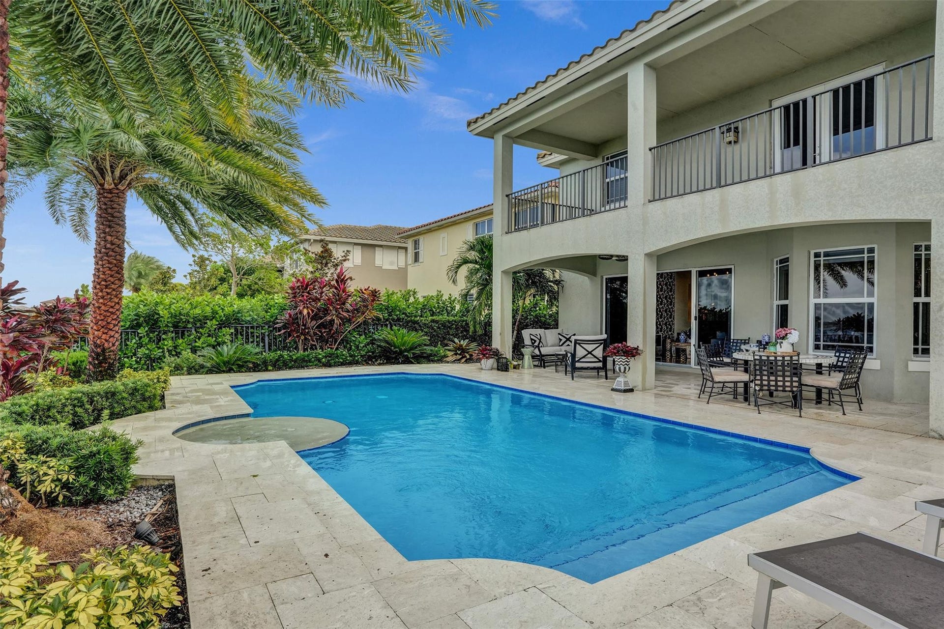 9749 Blue Isle, #BAY, Parkland, FL 33076 Expansive outdoor living area featuring a rectangular pool with integrated spa, surrounding travertine-style paving, and a covered patio