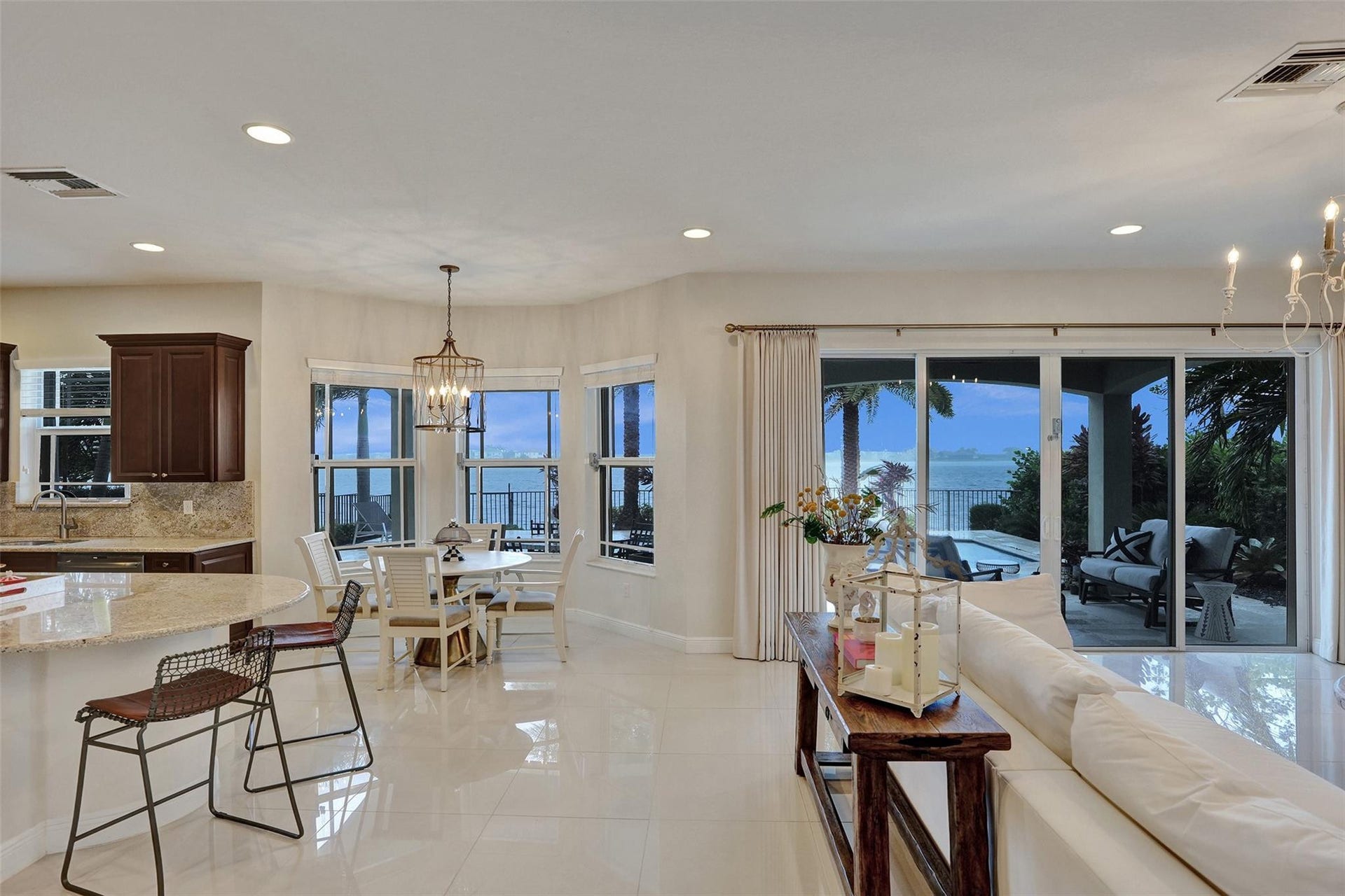 9749 Blue Isle, #BAY, Parkland, FL 33076 Expansive living area with high gloss tile flooring, recessed lighting, a built-in kitchen island with a stone countertop, a dining area with a multi-pane window, and sliding glass doors opening to an outdoor patio with a body of water beyond