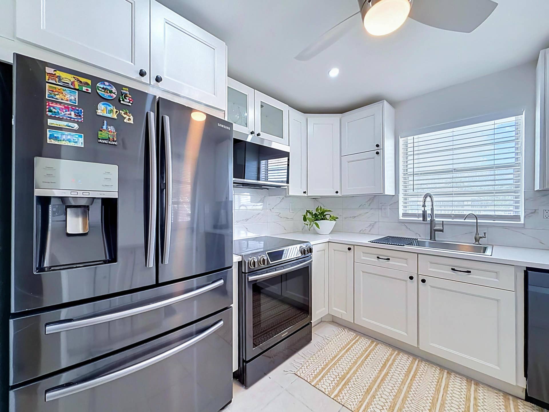 Kitchen featuring white shaker-style cabinetry, stainless steel appliances, a ceiling fan with integrated lighting, and a window with horizontal blinds