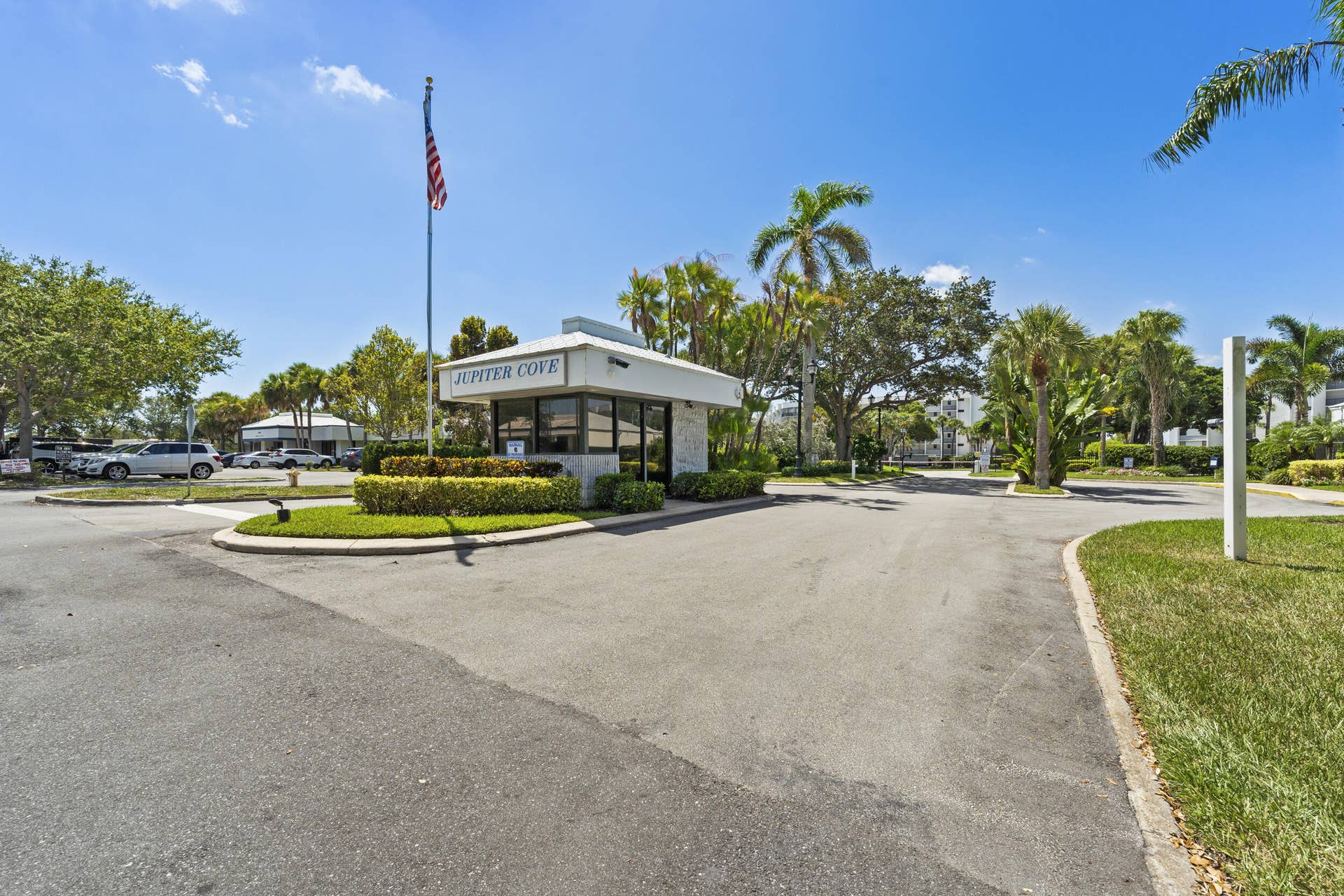 Gated community entrance featuring a guardhouse, mature landscaping, and an American flag