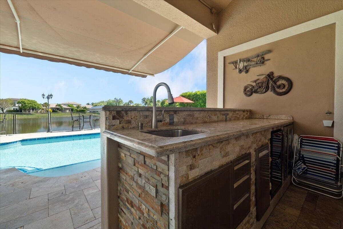 12390 NW 78th Manor, Parkland, FL 33076 The Outside stone built cocktail bar with stainless sink and all top of the line plumbing chrome fixtures and faucests, Stainless wine cooler/fridge & sink, Granite Bar top, A beautiful 18 x 10 foot electric remote controlled Retractable awning for cocktail shading & swimming, Crown moldings and custom wall enclose this cocktail bar area for full entertaiment