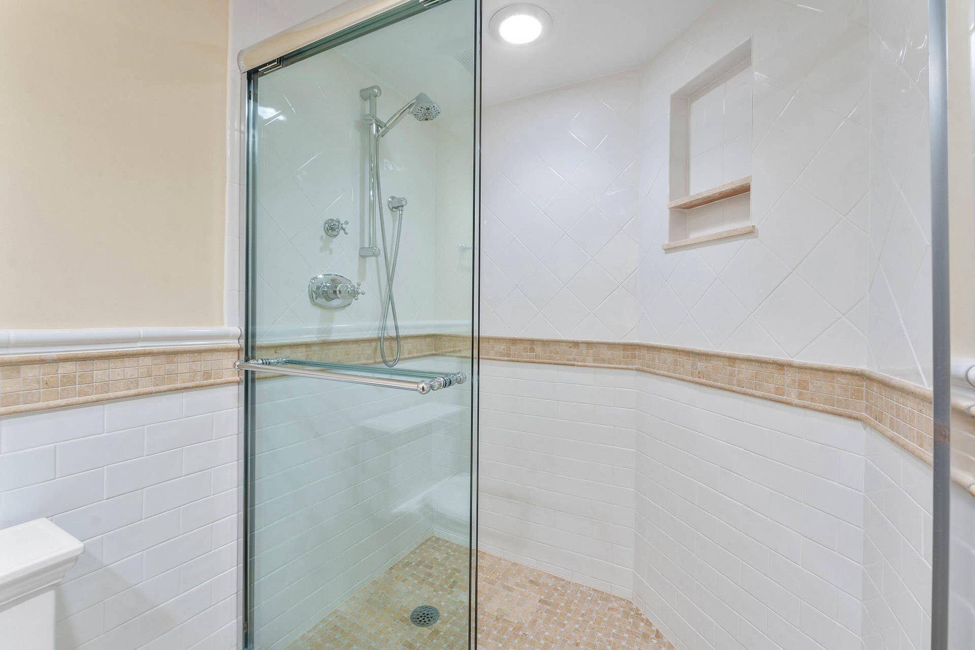A glass-enclosed shower with tiled walls and built-in niche completes the bath.