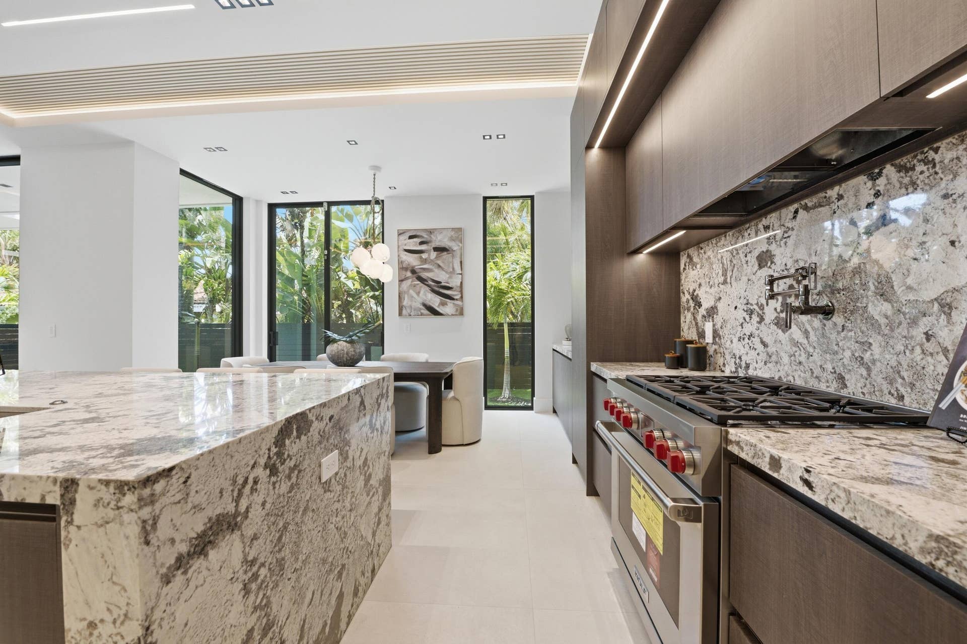 Kitchen featuring a professional-grade range, full-height stone backsplash, custom cabinetry, under-cabinet lighting, and a large stone island
