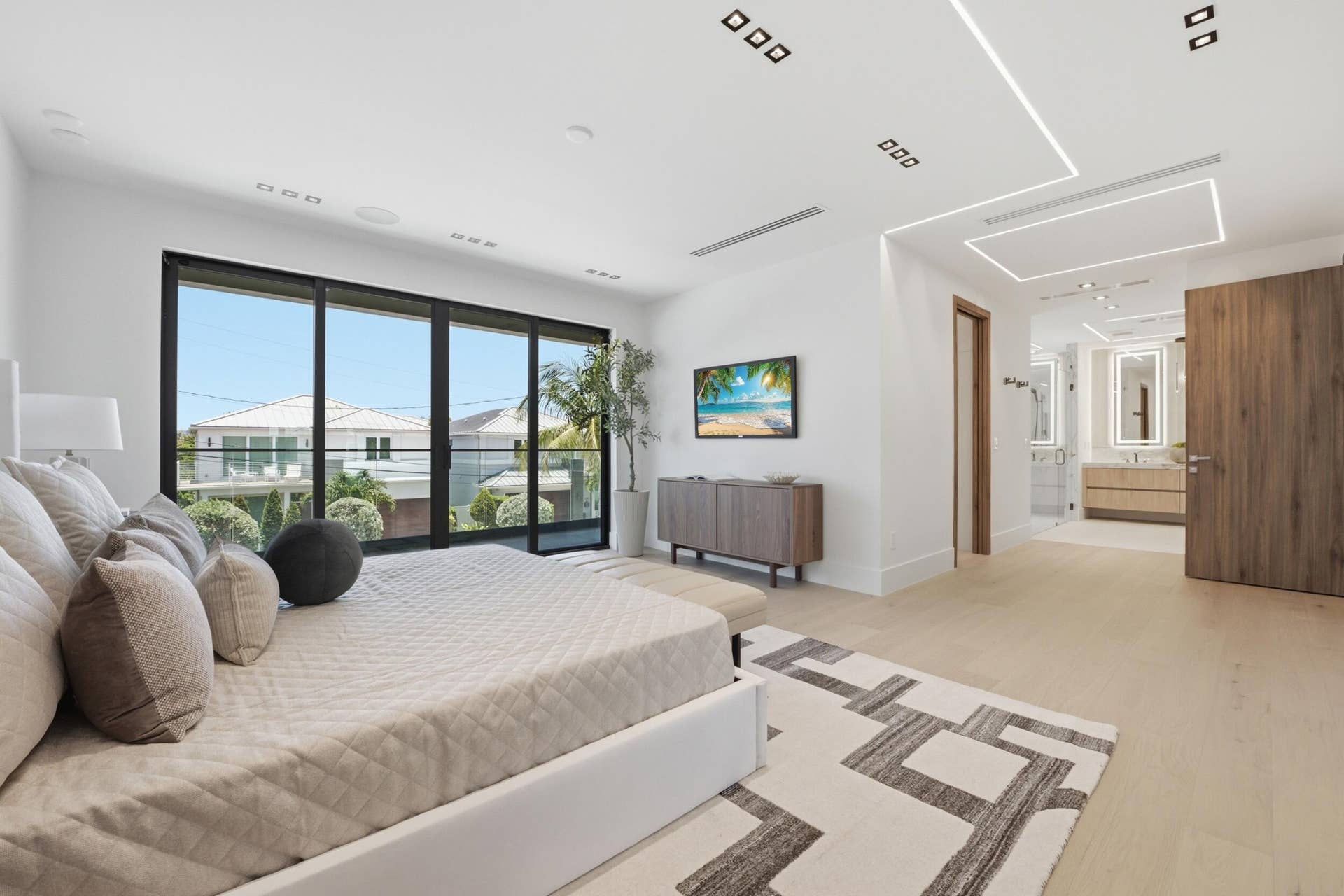Wide plank wood-finish flooring, recessed ceiling lighting, full-height sliding glass panel door, light wood bathroom vanity with dual sinks, and an integrated lighting fixture