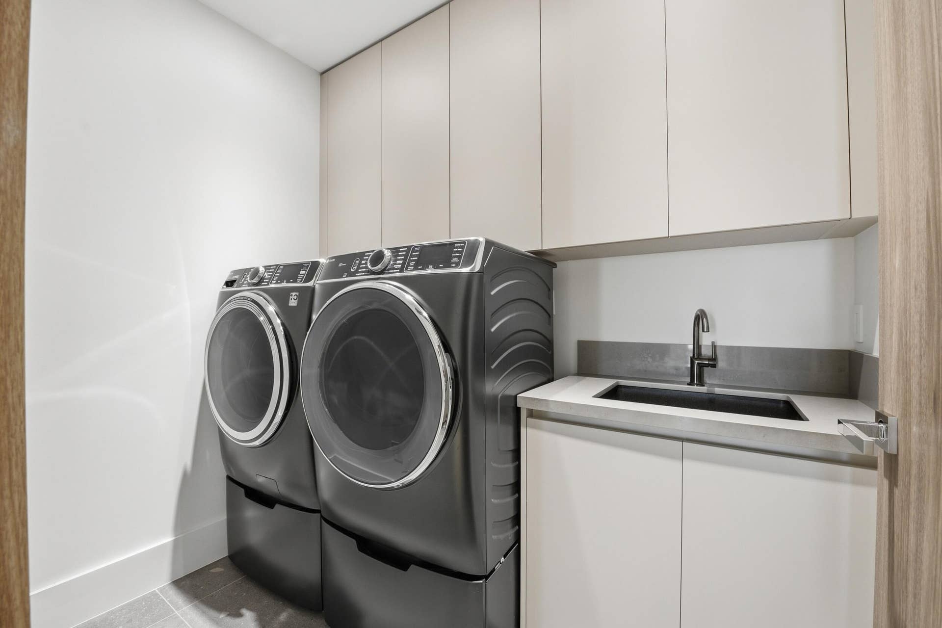 Integrated laundry appliances, built-in cabinetry, under-mount sink, matte black faucet, and light-toned countertop