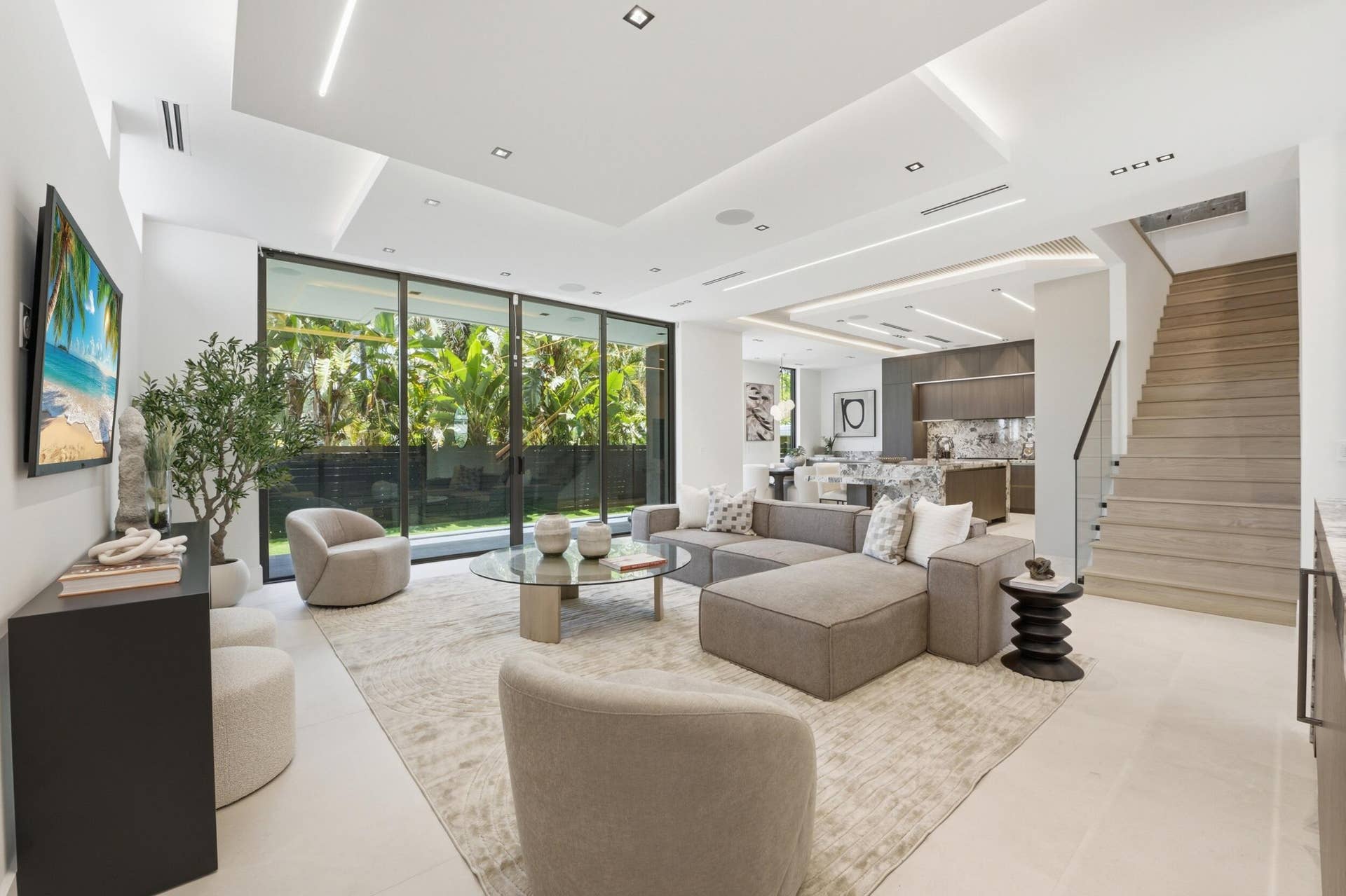 Recessed lighting with layered ceiling design, floor-to-ceiling sliding glass doors, light-toned flooring, wood-finish staircase, and open concept living area