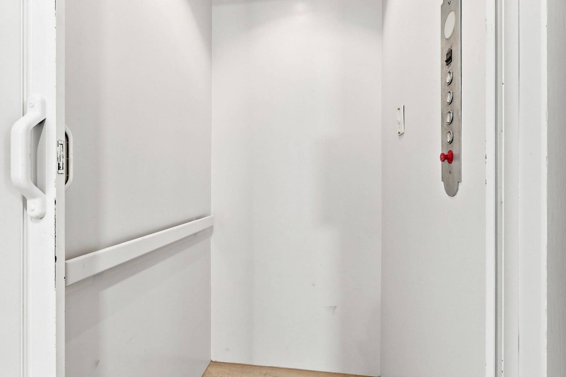 Interior elevator with luxury vinyl flooring, recessed ceiling lighting and a metal control panel featuring red emergency stop button