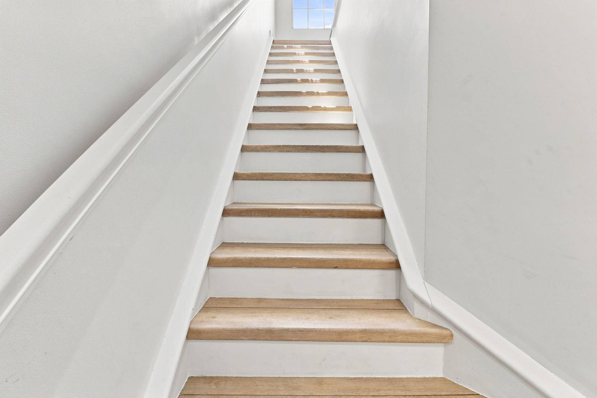 Staircase featuring wood-finish treads and risers, bright walls and a window