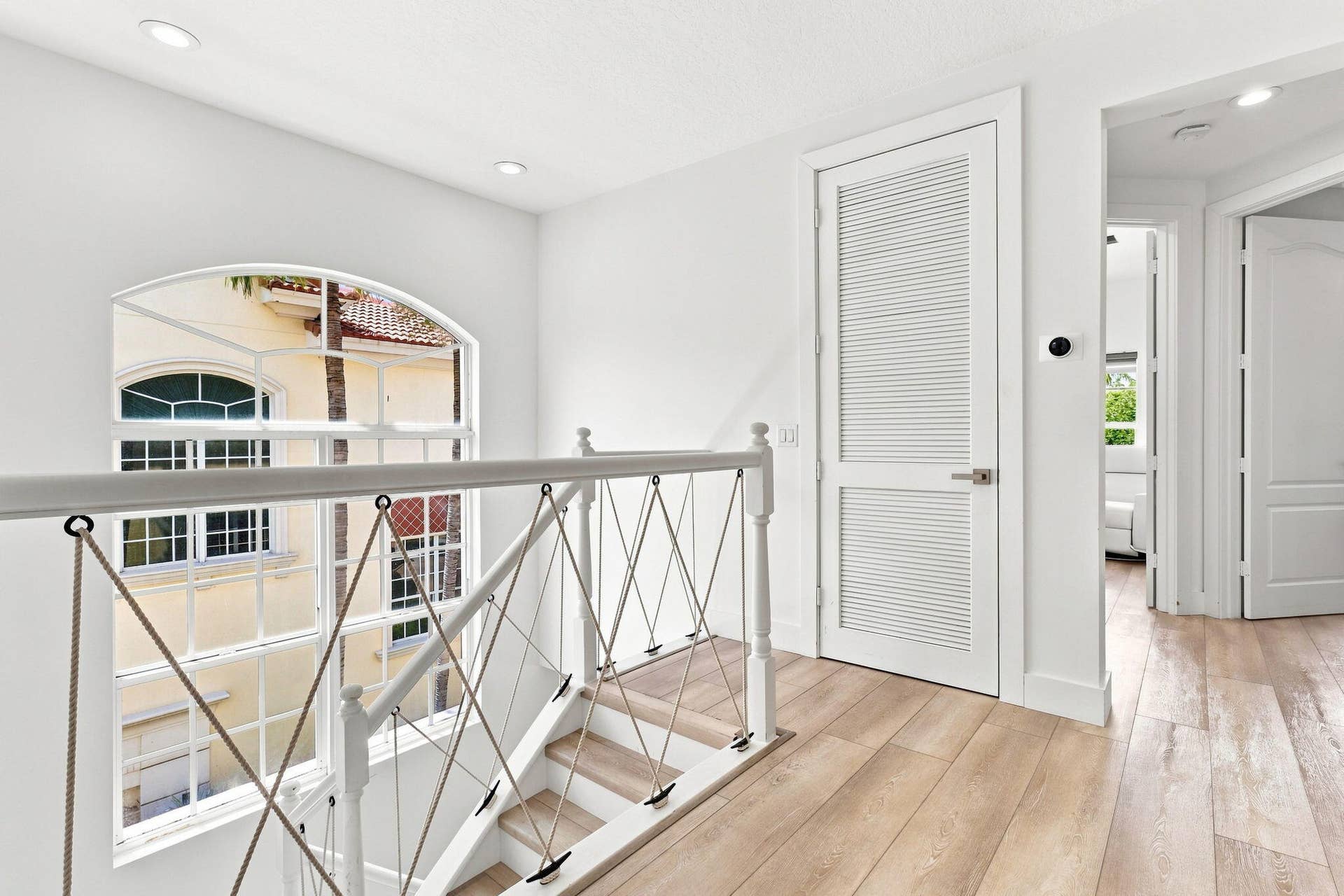 Arched window with multiple panes, luxury vinyl flooring, white louvered door, recessed lighting and a contemporary cable railing system