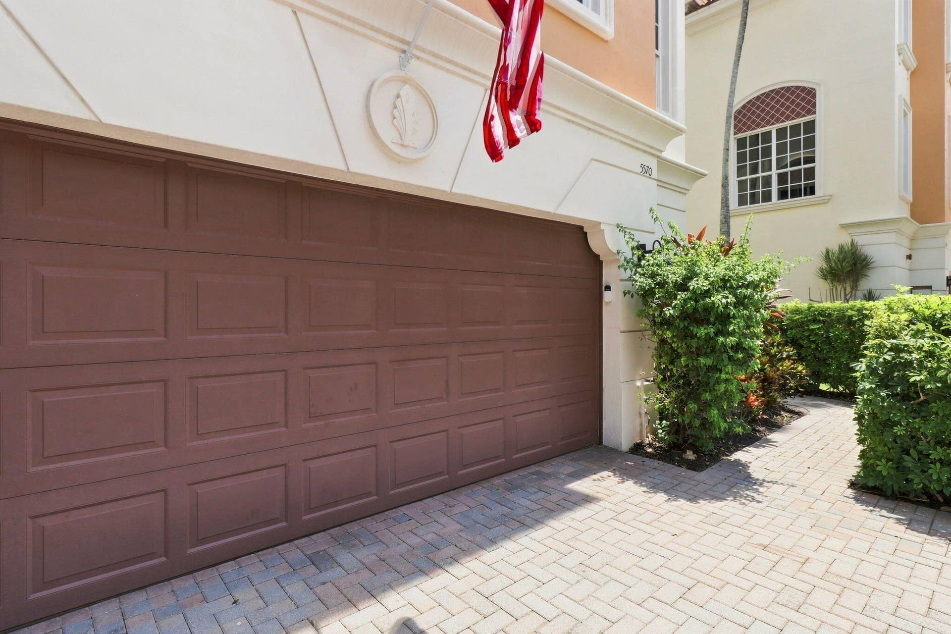 Paver driveway with a panel-style garage door and manicured landscaping