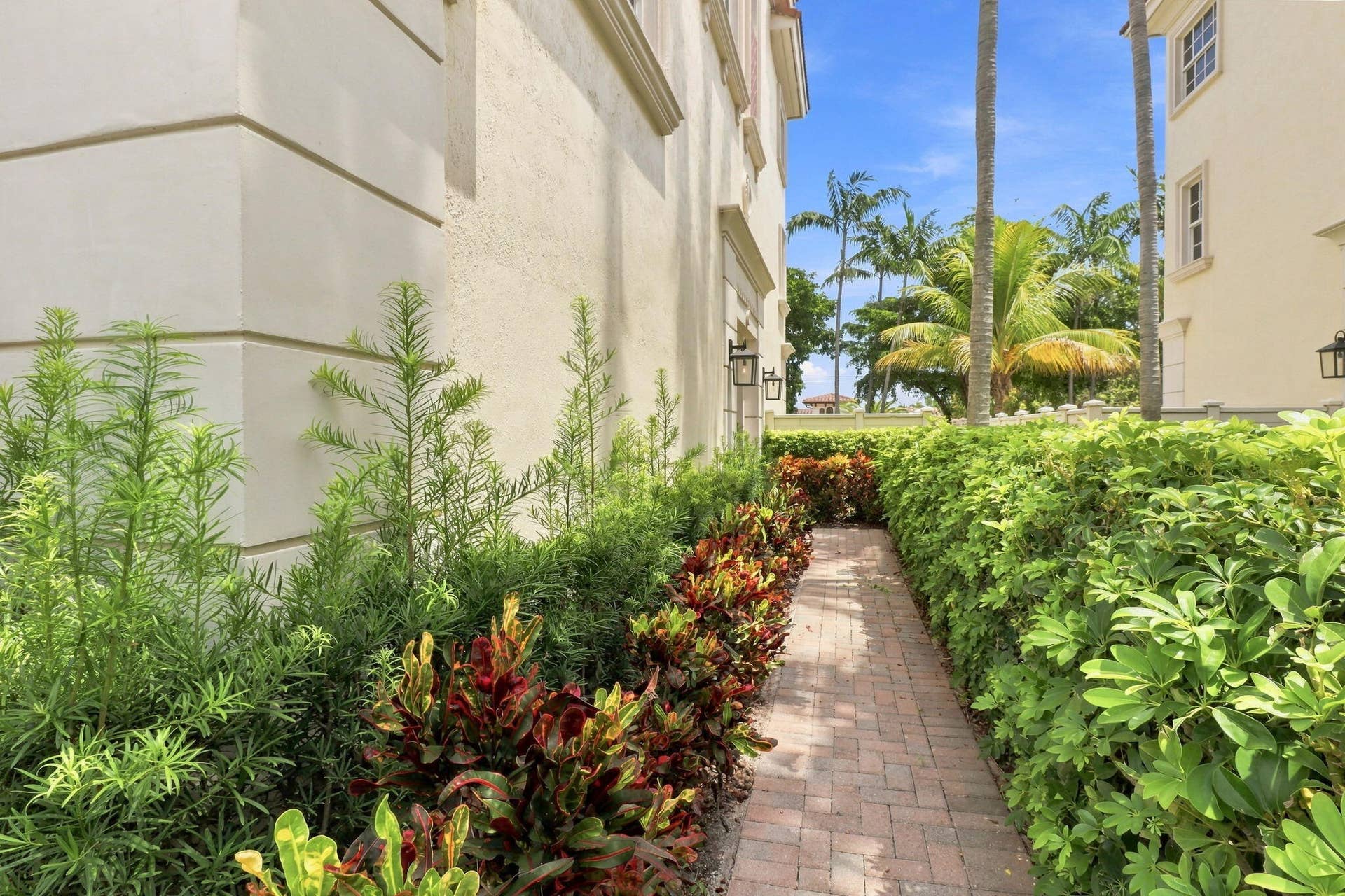 Brick paver pathway with mature tropical landscaping and exterior wall sconces