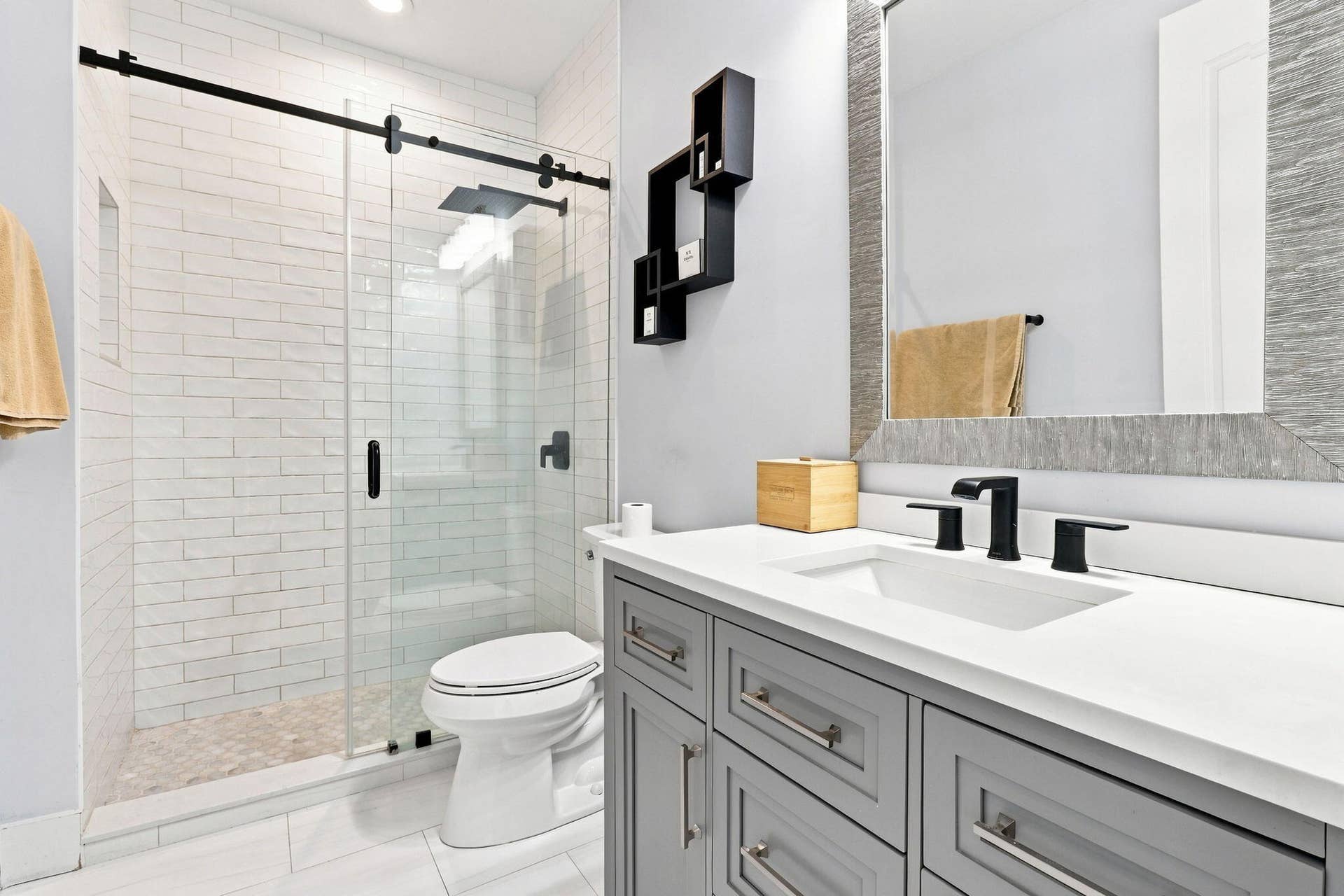 Glass-enclosed shower with subway tile surround and dark hardware, vanity with a white countertop and undermount sink and tile flooring