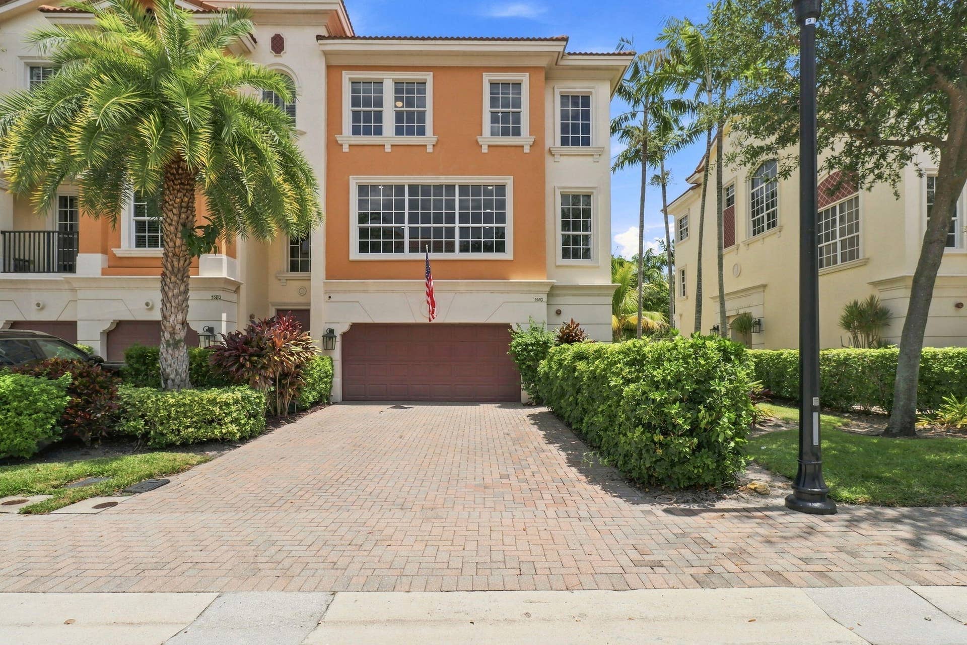 Stucco exterior with multiple windows, an integrated garage, a paver driveway and mature landscaping