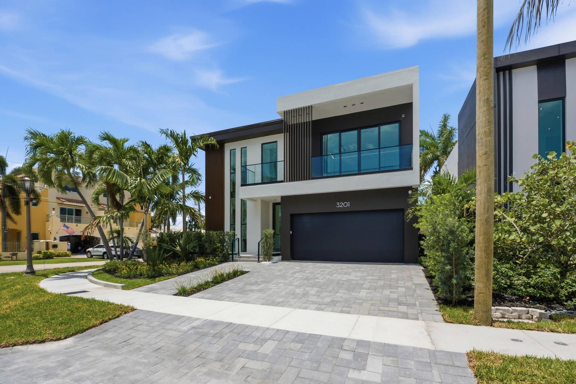 Contemporary two-story exterior with a flat roofline, an integrated garage, a paved driveway, a second-story balcony with a glass railing, and a ground-floor entry with a dark door
