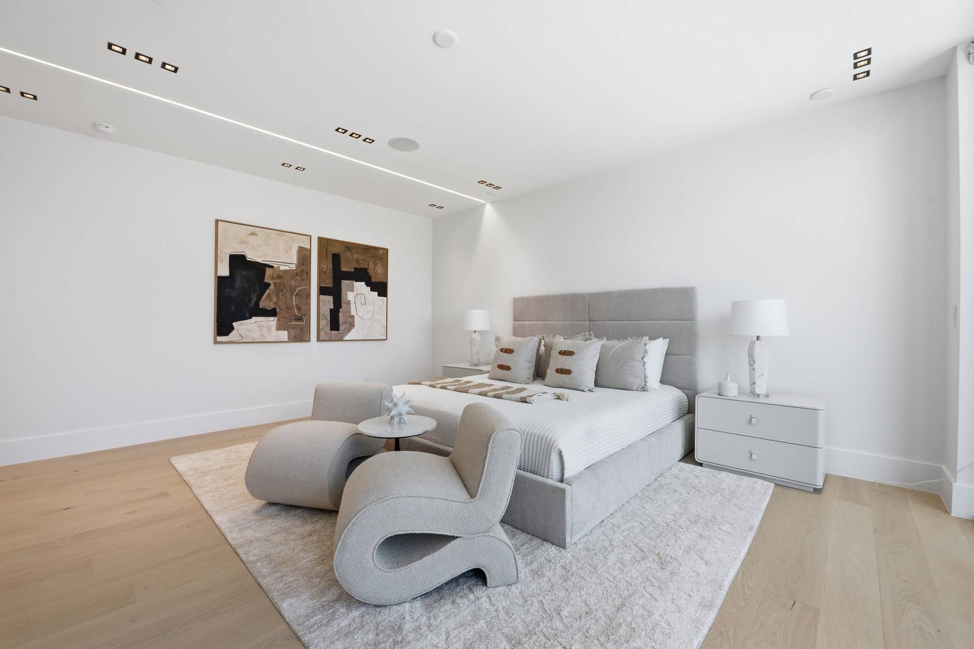 Recessed ceiling lighting, linear ceiling lighting, light wood-finish flooring, white walls, and a built-in upholstered headboard