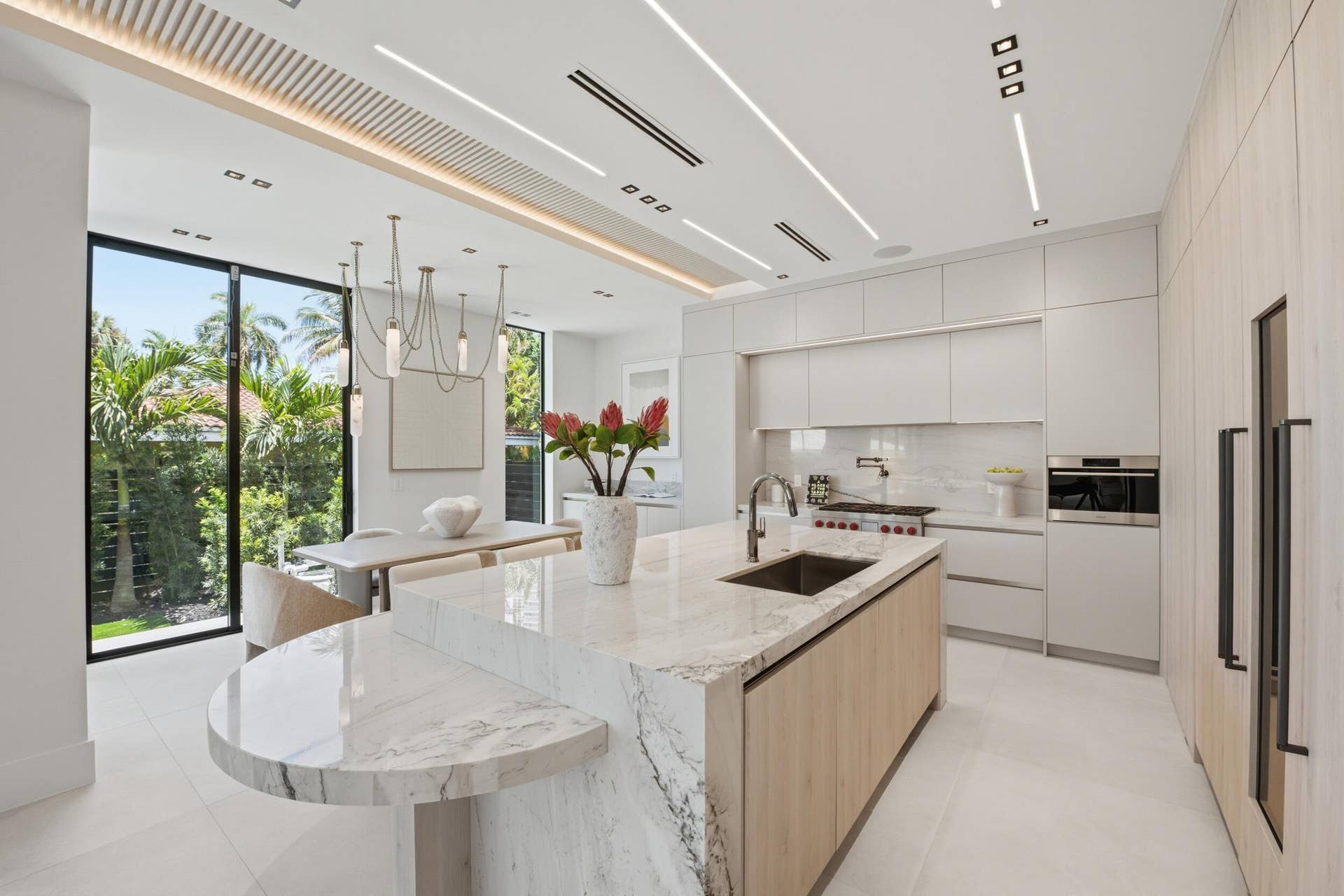 Gourmet kitchen featuring a waterfall island, integrated appliances, white cabinetry, and extensive full-height windows