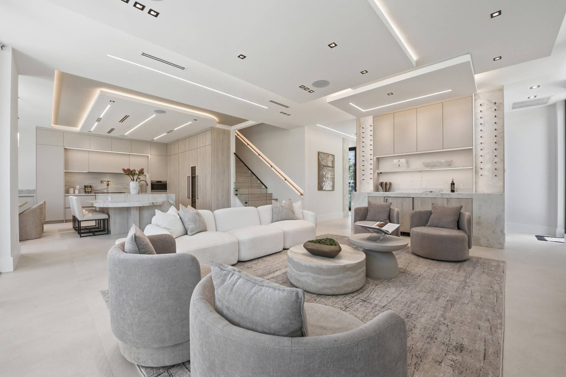 Open-concept living space featuring a built-in wet bar, gourmet kitchen with island, and a modern staircase with a black handrail