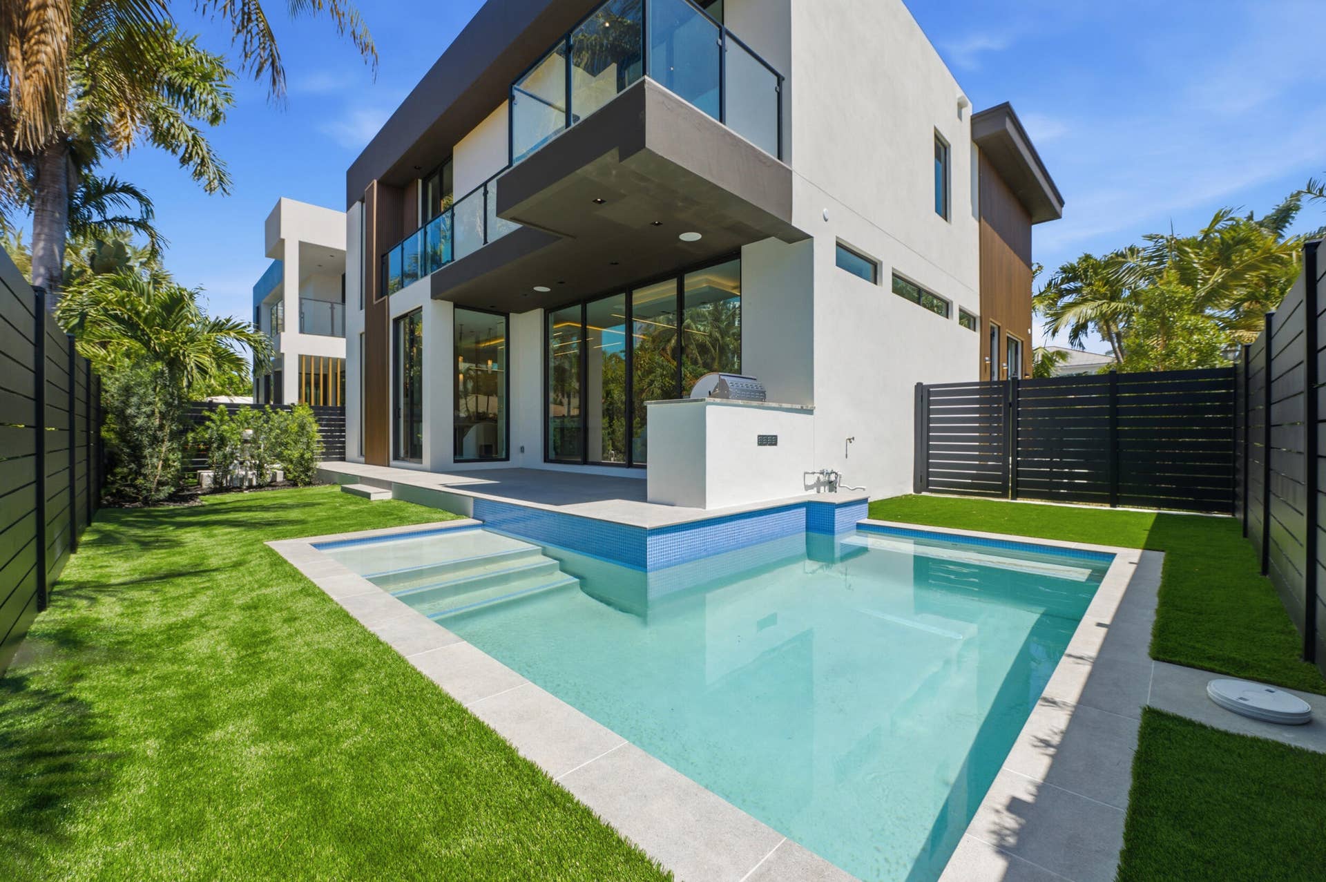 Contemporary exterior with a private swimming pool, built-in outdoor kitchen, expansive glass doors, second-story balcony with glass railing, and a manicured lawn