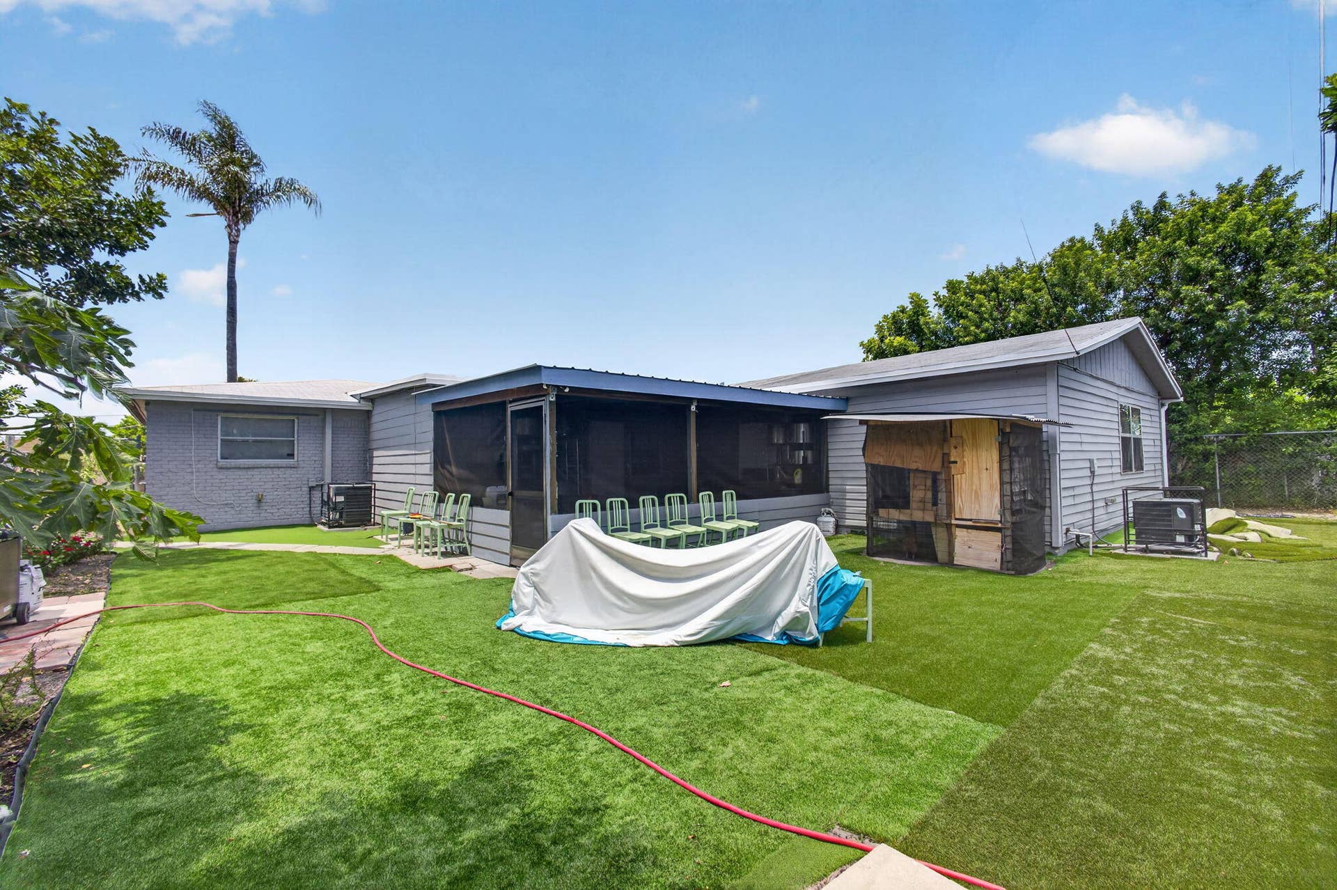 Expansive backyard featuring artificial turf, a screened-in patio, and a dedicated utility shed