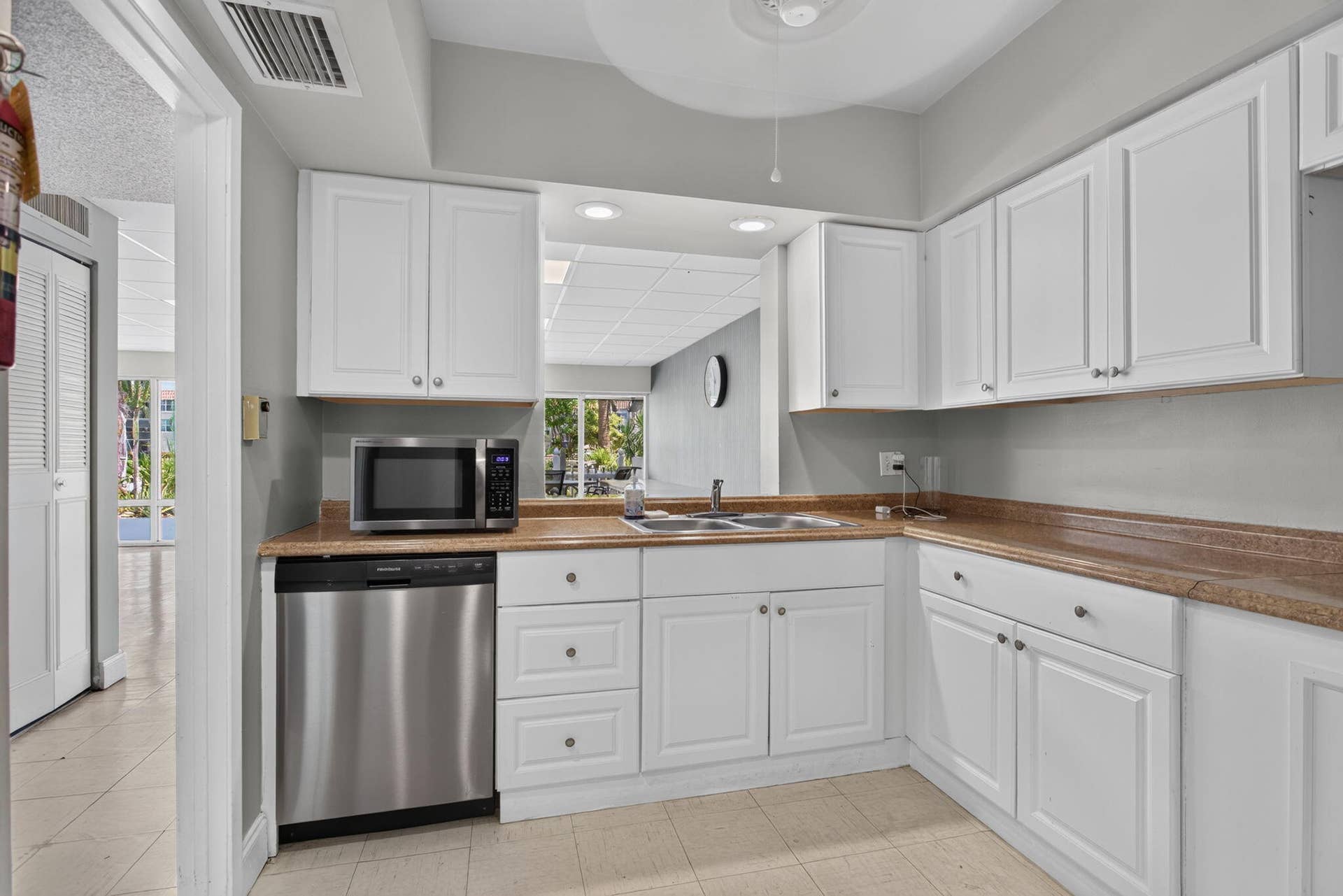 801 S Federal Highway, #1103, Pompano Beach, FL 33062 Kitchen featuring white cabinetry, light-toned countertops, a stainless steel dishwasher, and a pass-through window