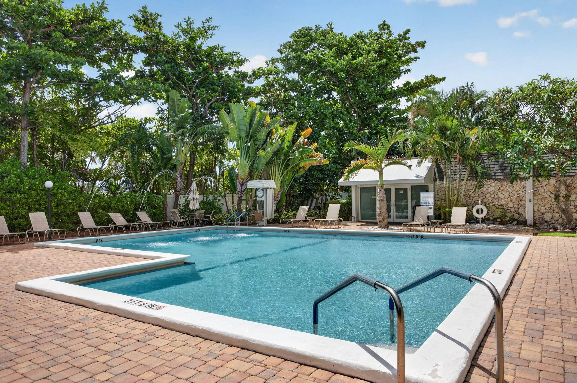 801 S Federal Highway, #1103, Pompano Beach, FL 33062 Rectangular swimming pool with integrated water features, surrounded by a paver deck, lush tropical landscaping, and a poolside cabana