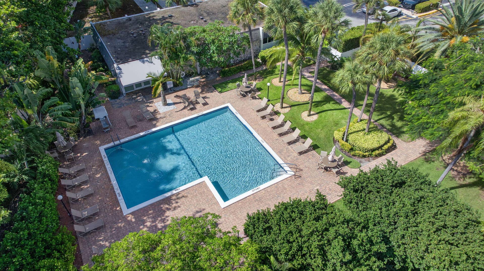 801 S Federal Highway, #1103, Pompano Beach, FL 33062 Rectangular swimming pool with a corner entry, surrounded by a brick paver deck, lush landscaping, and mature palm trees
