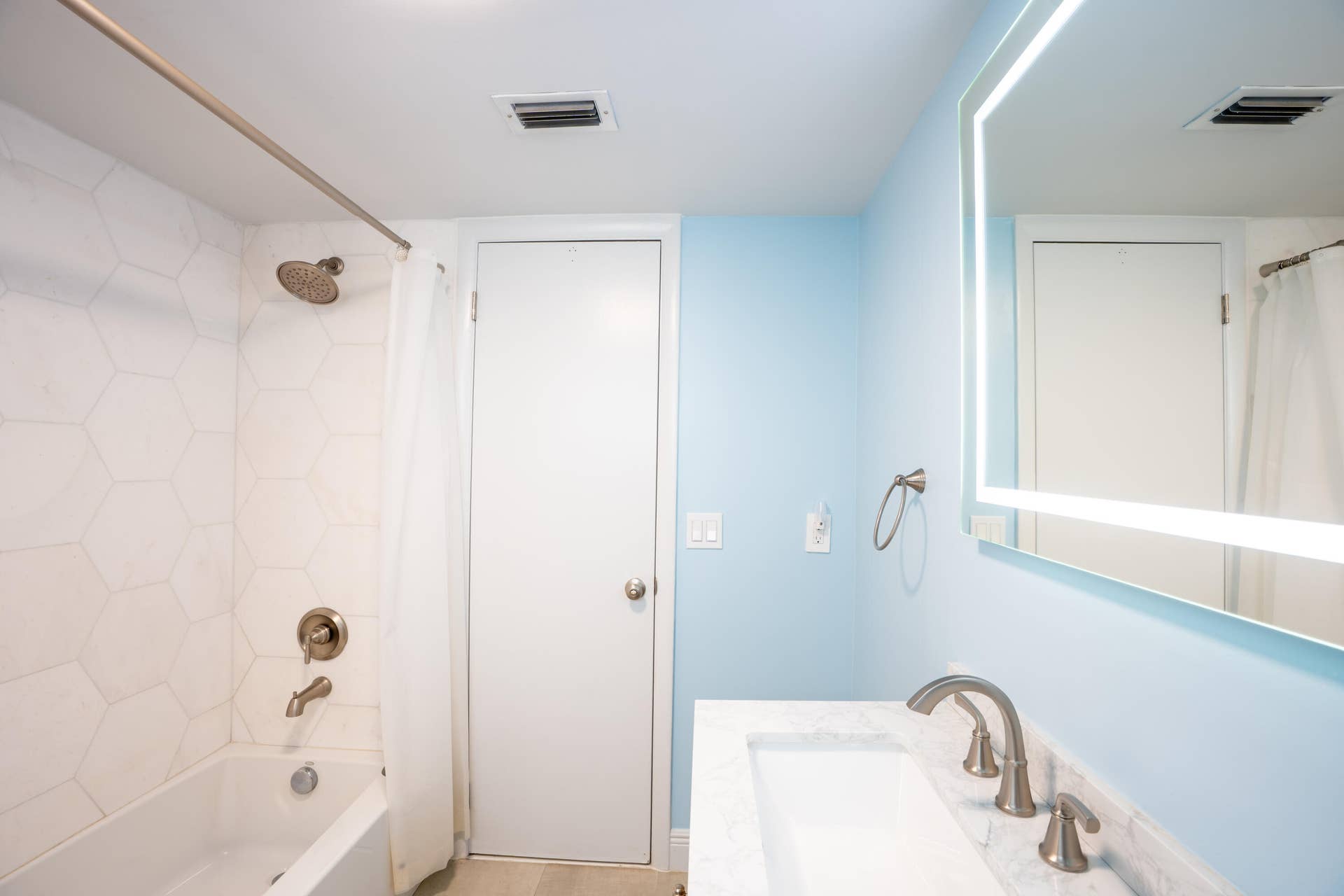 17 SE 8TH Terrace, Deerfield Beach, FL 33441 Bathtub with hexagonal tile surround, brushed nickel shower fixtures, vanity with integrated rectangular sink, marble-finish countertop, and illuminated mirror