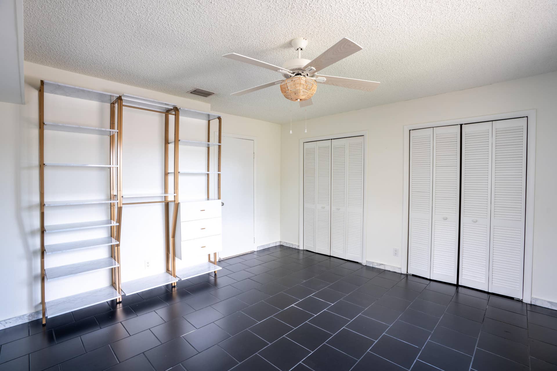 17 SE 8TH Terrace, Deerfield Beach, FL 33441 Black tile flooring, built-in shelving system with hanging rods and drawers, two louvered bifold closet doors, white ceiling fan, and white walls