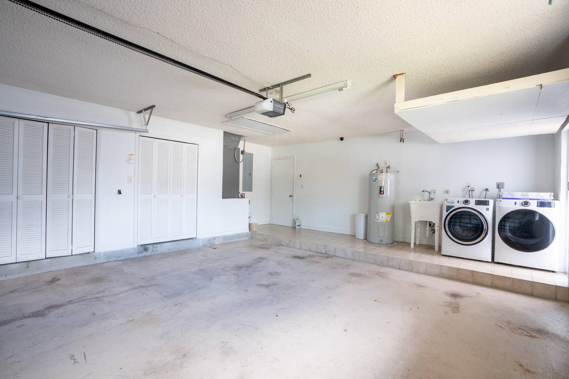 17 SE 8TH Terrace, Deerfield Beach, FL 33441 Spacious garage with polished concrete flooring, white overhead sectional door, ceiling fan, and dedicated laundry alcove featuring side-by-side washer and dryer units