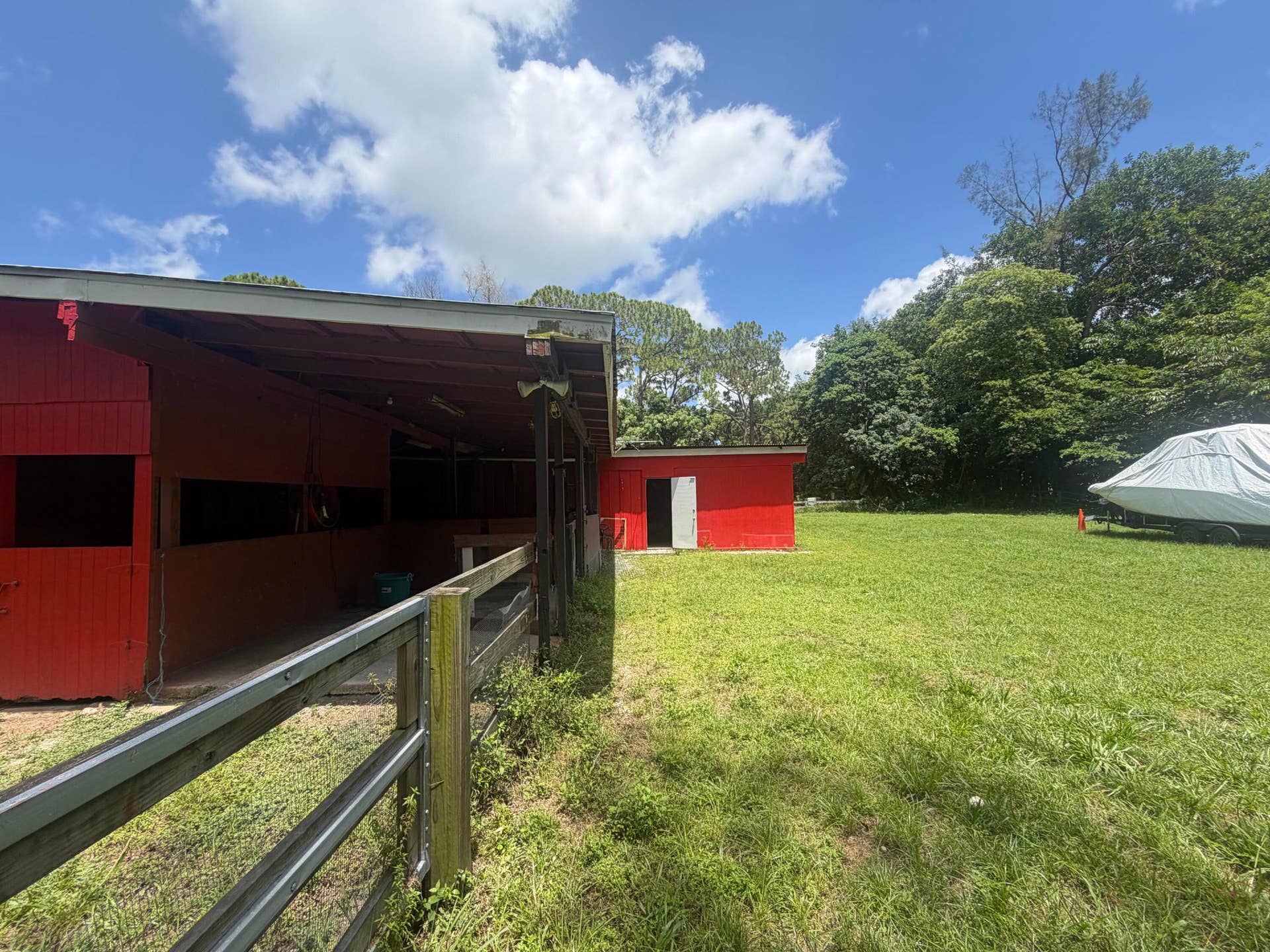 4020 Vinkemulder Road, Coconut Creek, FL 33073 Red stable structure with multiple stalls, wood fencing, and a separate red outbuilding
