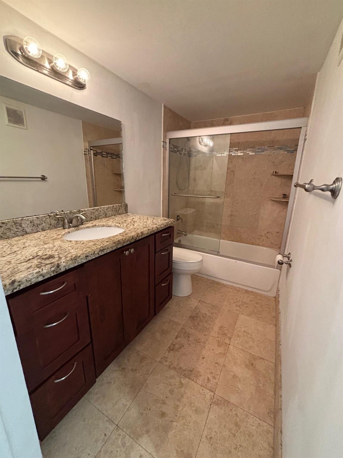 Granite countertop with integrated sink, wood-finish vanity cabinetry, tiled flooring, and a tub-shower combination with sliding glass doors
