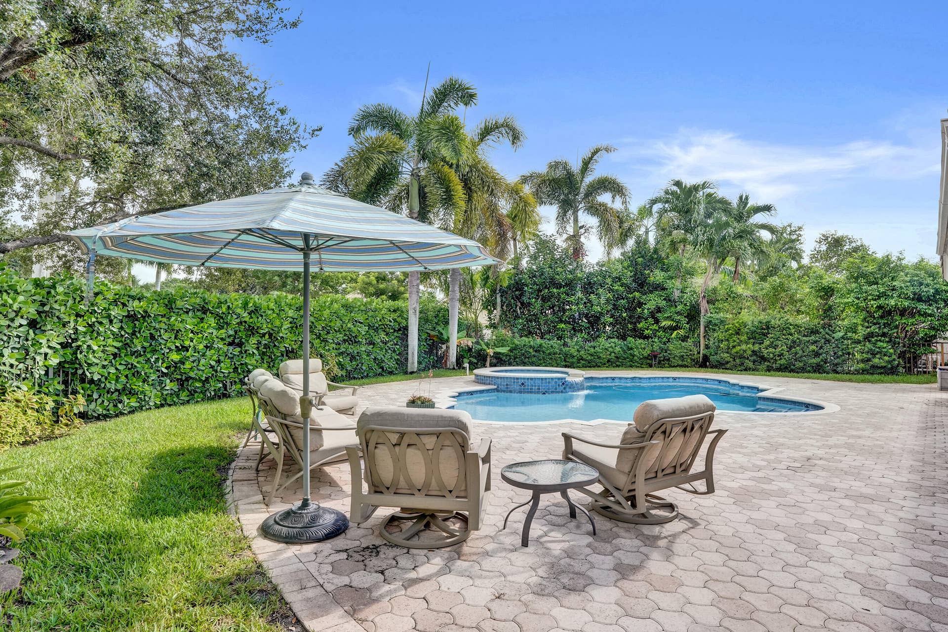 Shaped pool with integrated spa, paver patio, lush landscaping, and mature trees