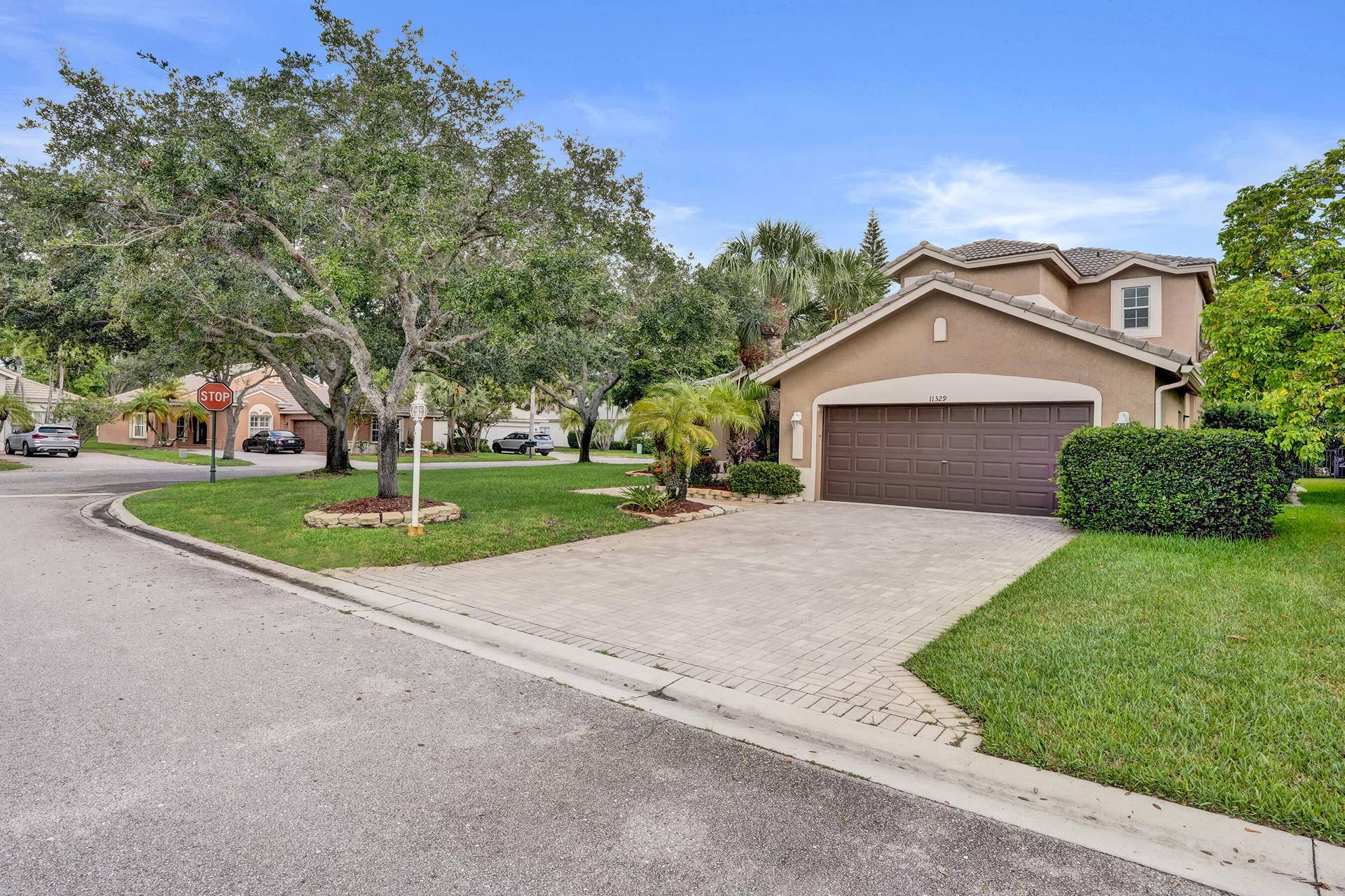 Stucco exterior with a tiled roof, two-car garage, paver driveway, and tropical landscaping