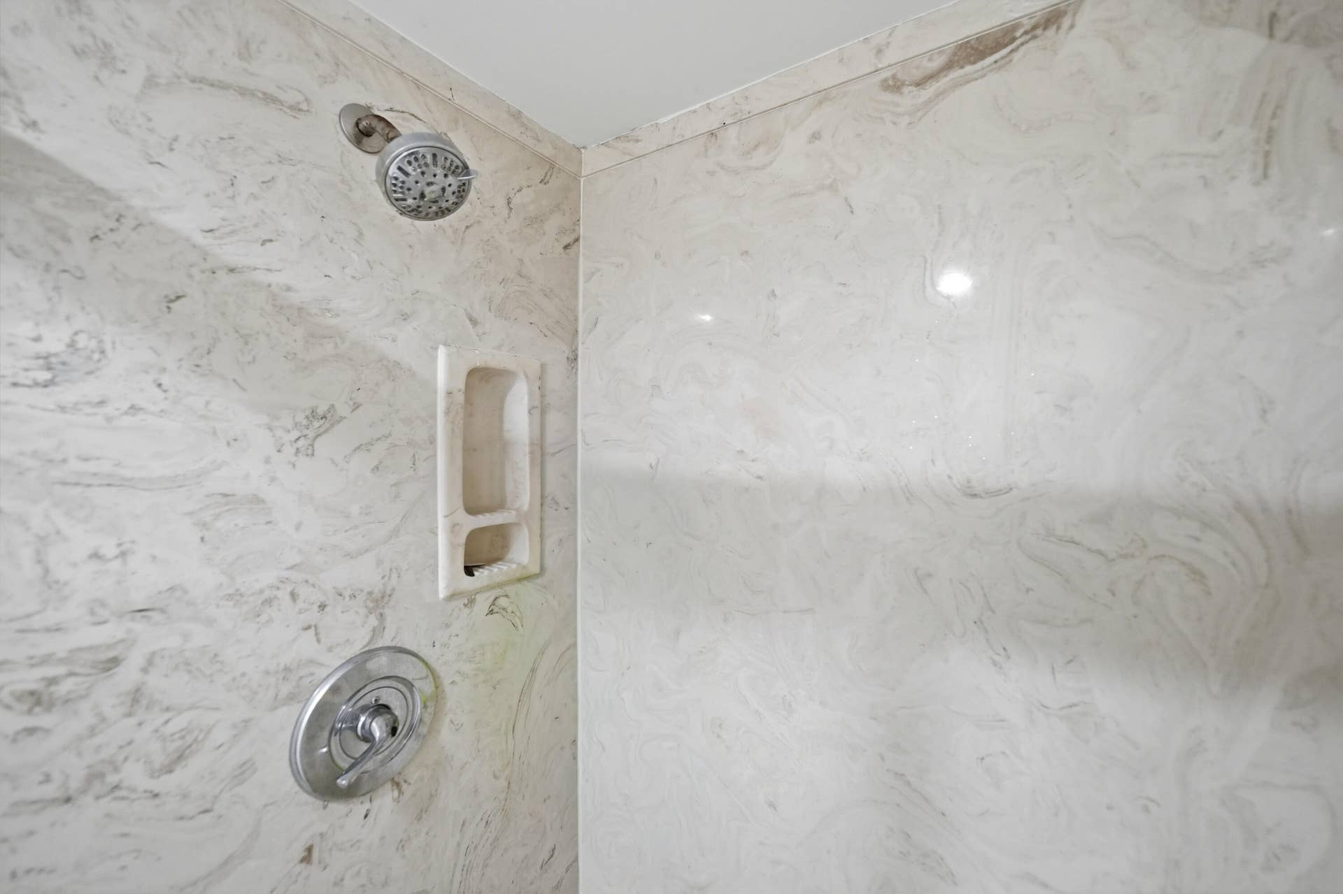 Shower enclosure with light-toned wall panels, a built-in shower niche, a chrome-finish shower head, and a matching shower control handle