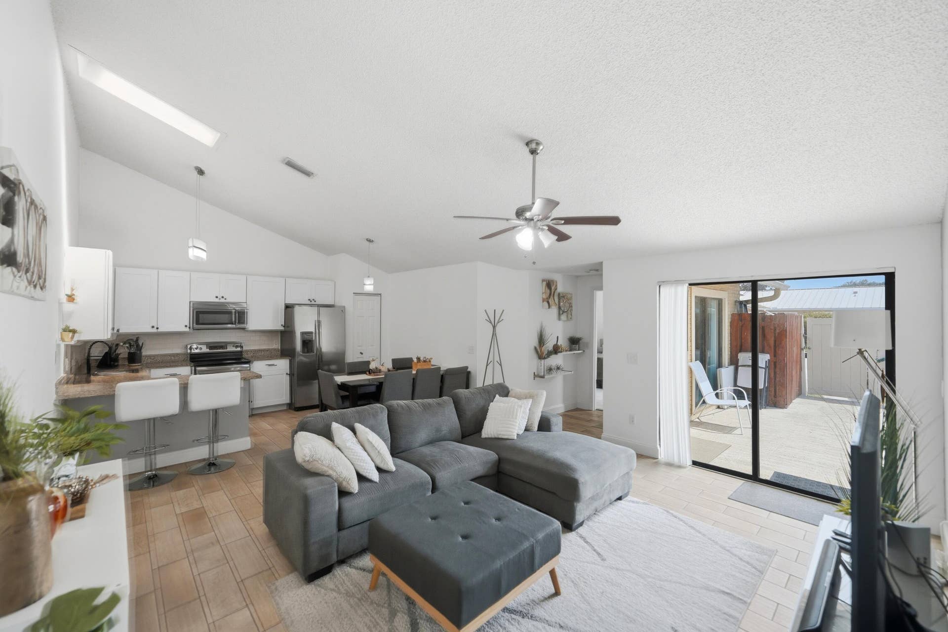 Vaulted ceiling with skylight, wood-finish flooring, white cabinetry with stainless steel appliances, breakfast bar, and sliding glass door to exterior patio