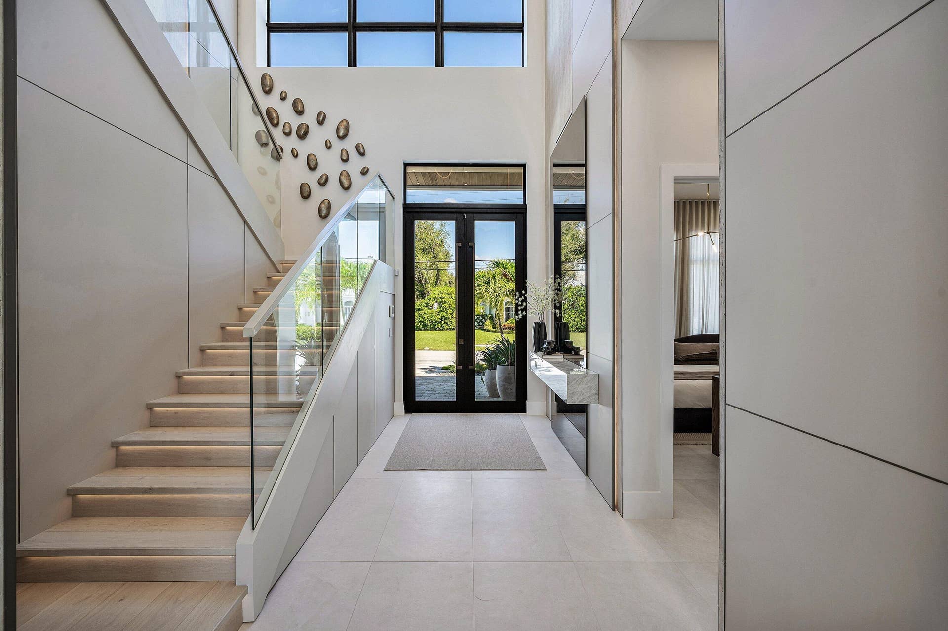 Grand entryway featuring a floating stone console, recessed lighting, glass railing staircase, and light-toned flooring