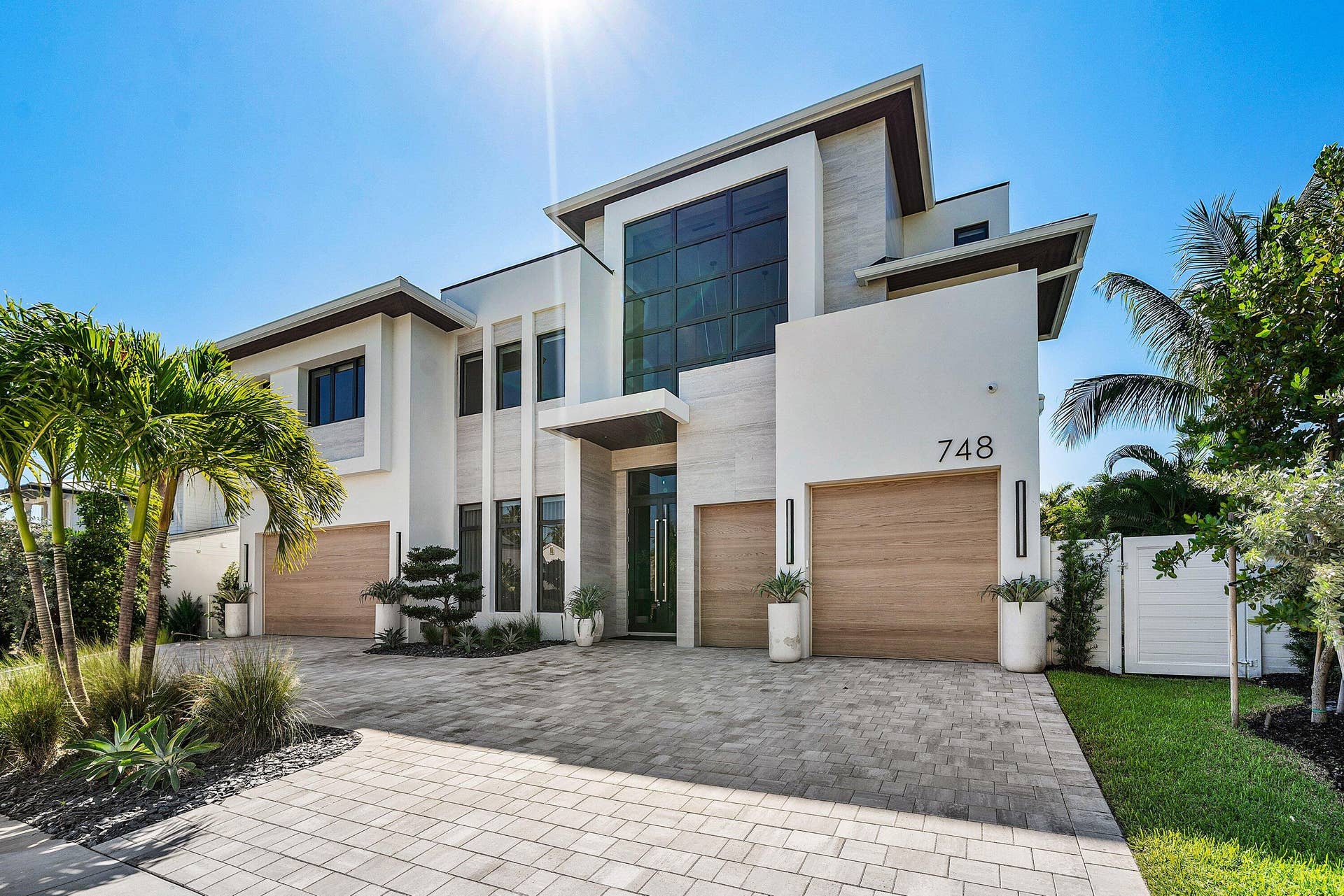 Contemporary stucco exterior with a flat roofline, wood-finish garage doors, large dark-framed windows, and a paver driveway