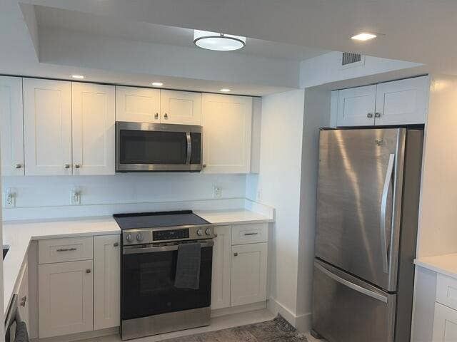 White shaker-style cabinetry with stainless steel hardware, white countertops, built-in microwave, stainless steel range, and stainless steel refrigerator